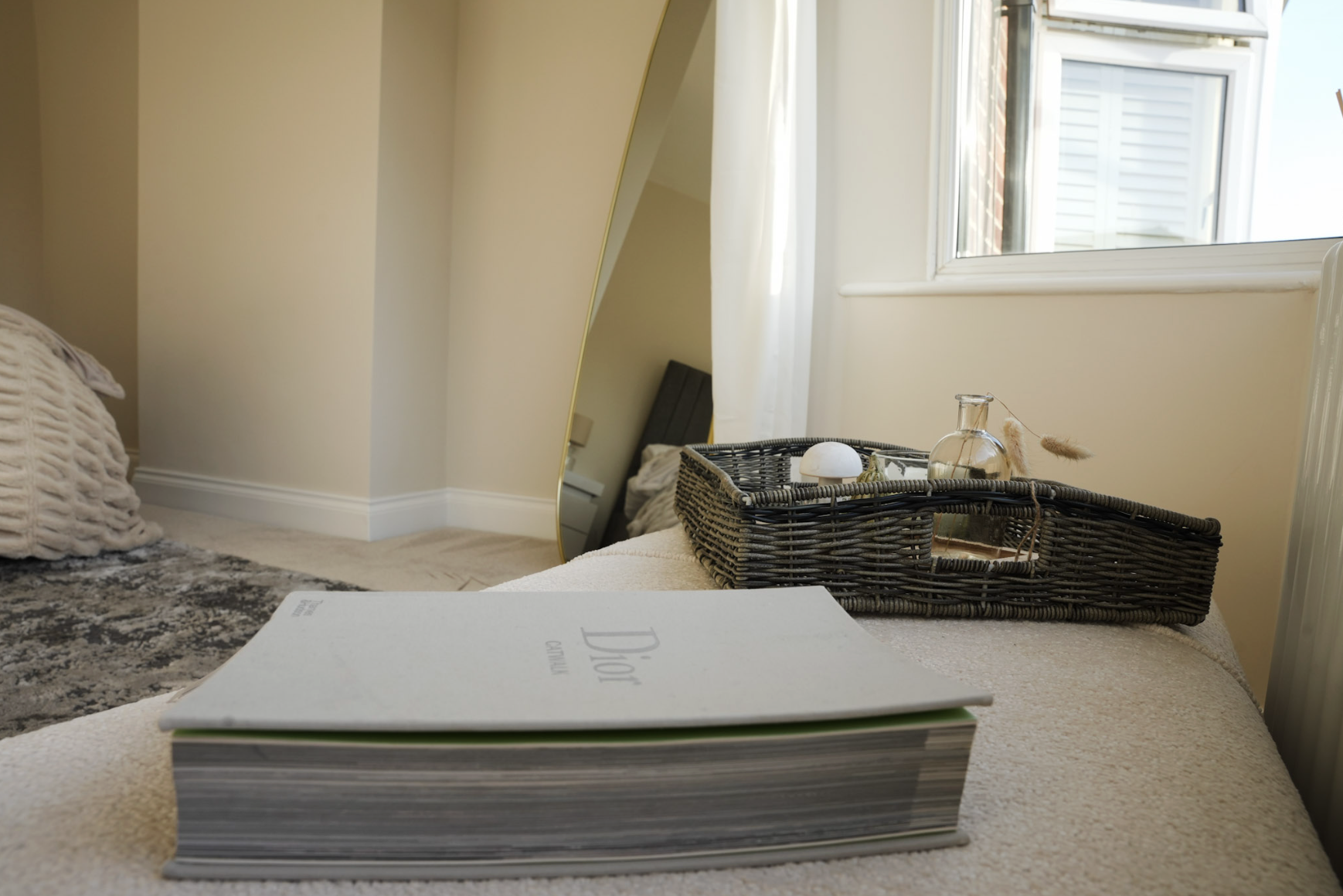 A bedroom with a large mirror, open window, and a tray with decorative items on a bed.