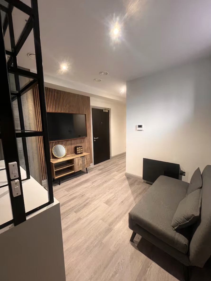 Modern living room with a gray sofa, wooden TV stand with a circular mirror, and a flat-screen TV on a wood-paneled accent wall.