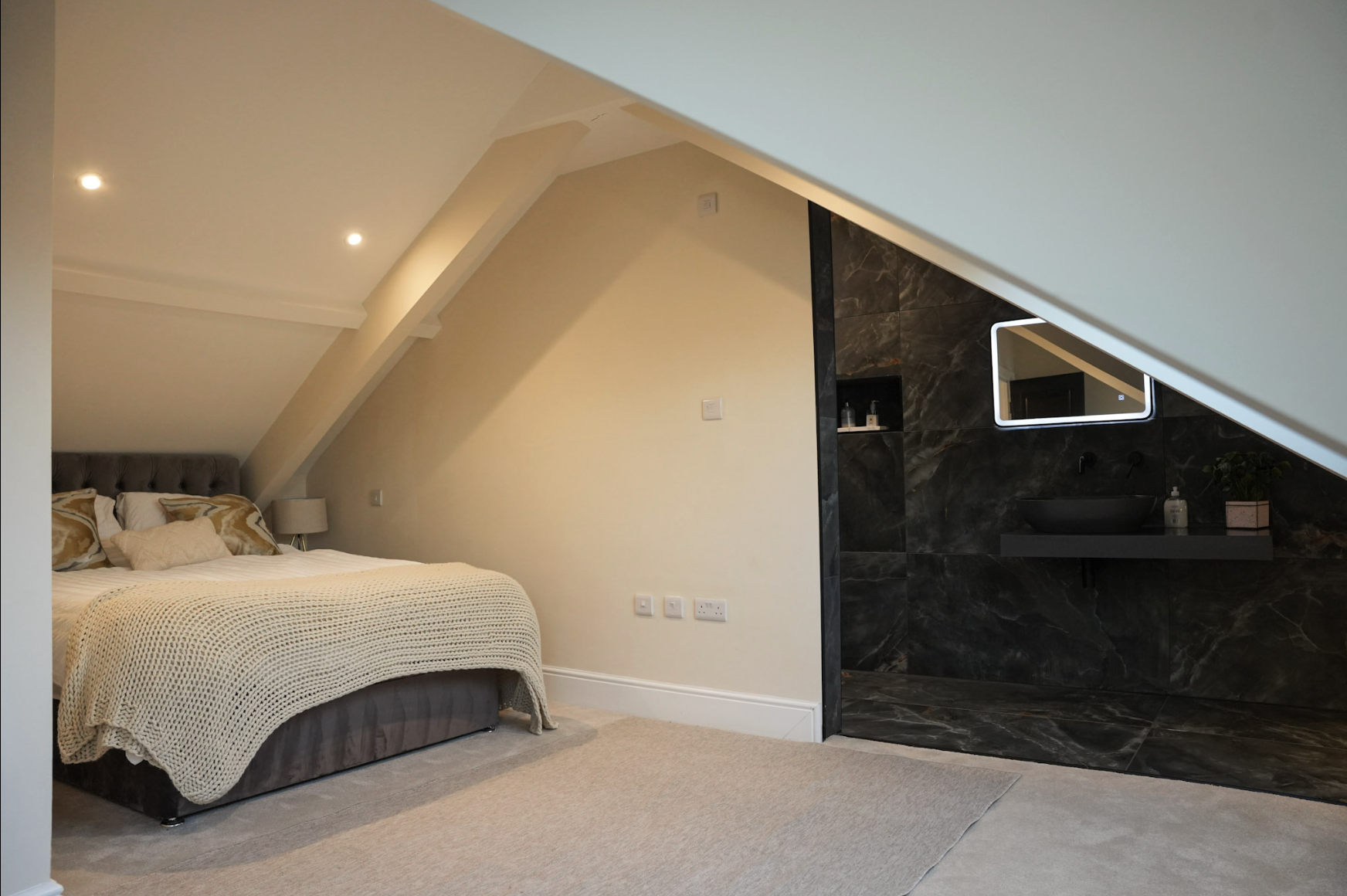 A bedroom with a bed near the left and an open walk-in closet or bathroom area with dark marble tiles on the right side of the room, under a sloped ceiling.