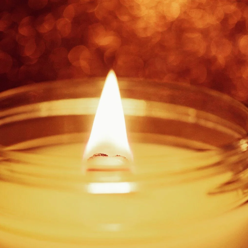 Close-up of a lit candle with a focused flame, blurred background with warm tones.