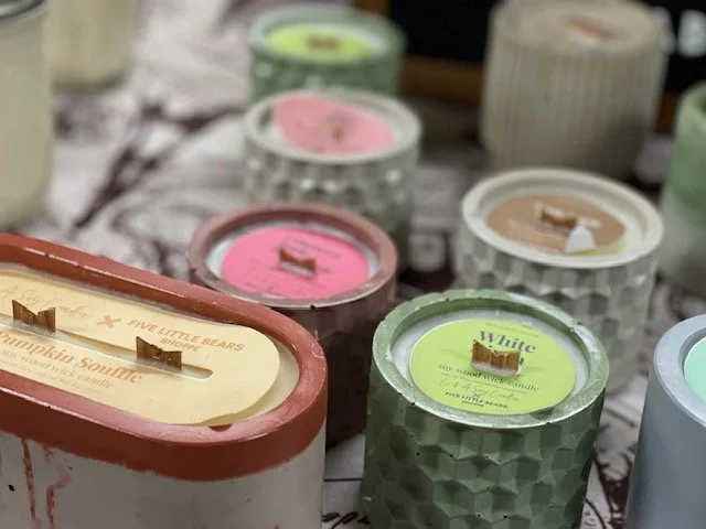 Various containers of soy wax candles in hand poured concrete vessels in different colors and flavors on a table.