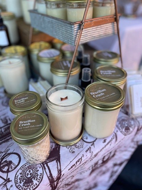 Various candles in glass jars on a table at a market stall, with some on a multi-tiered display.