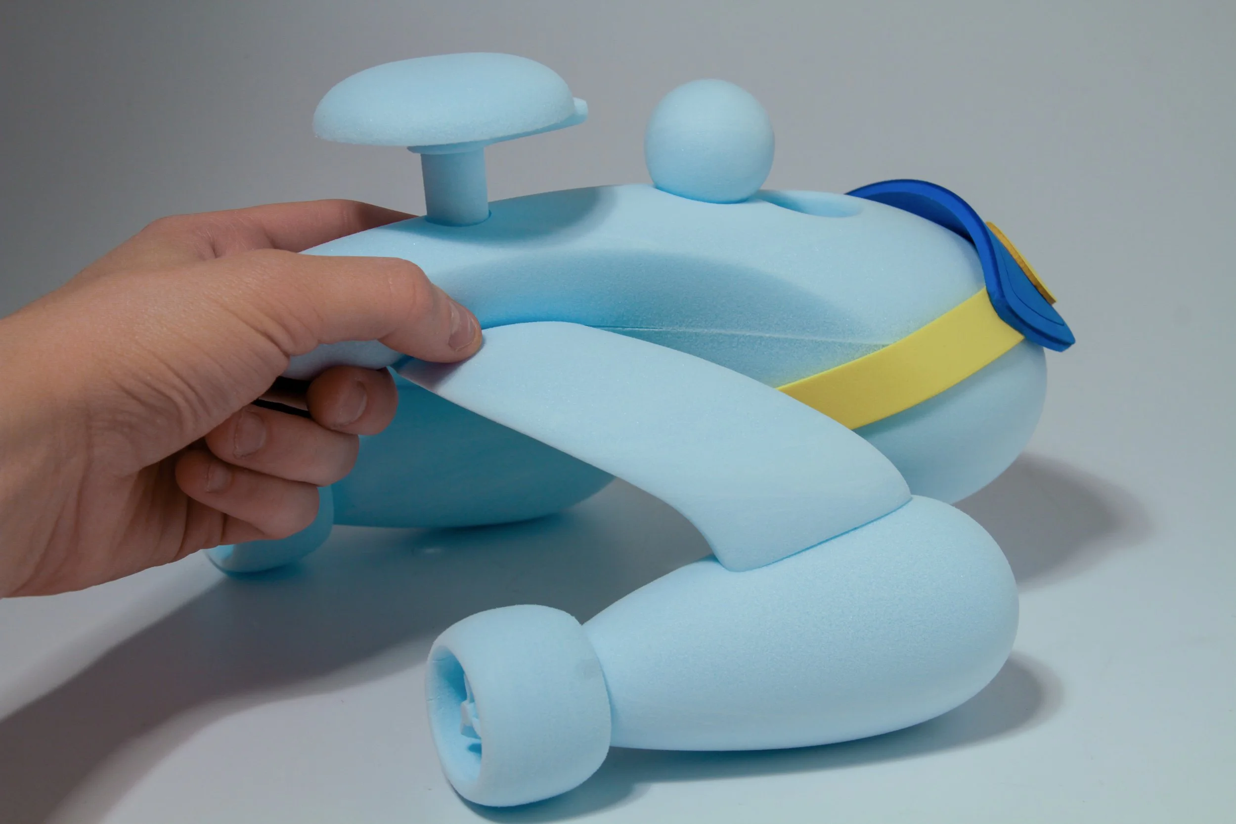 Blue foam toy shaped like a helicopter with a yellow stripe and blue details, being held by a person's left hand.
