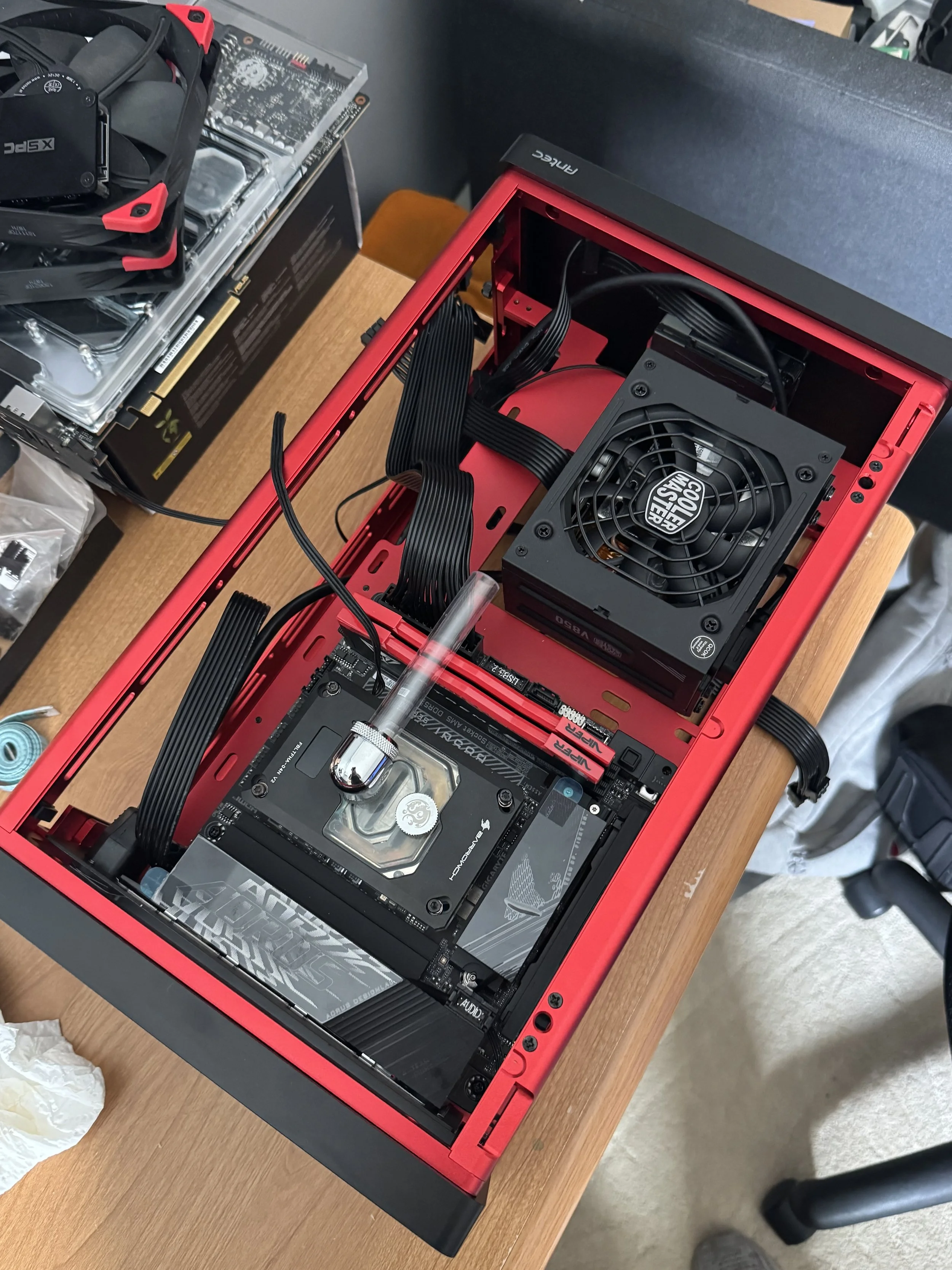 Open red PC case with installed graphics card, motherboard, and power supply, sitting on a wooden table.