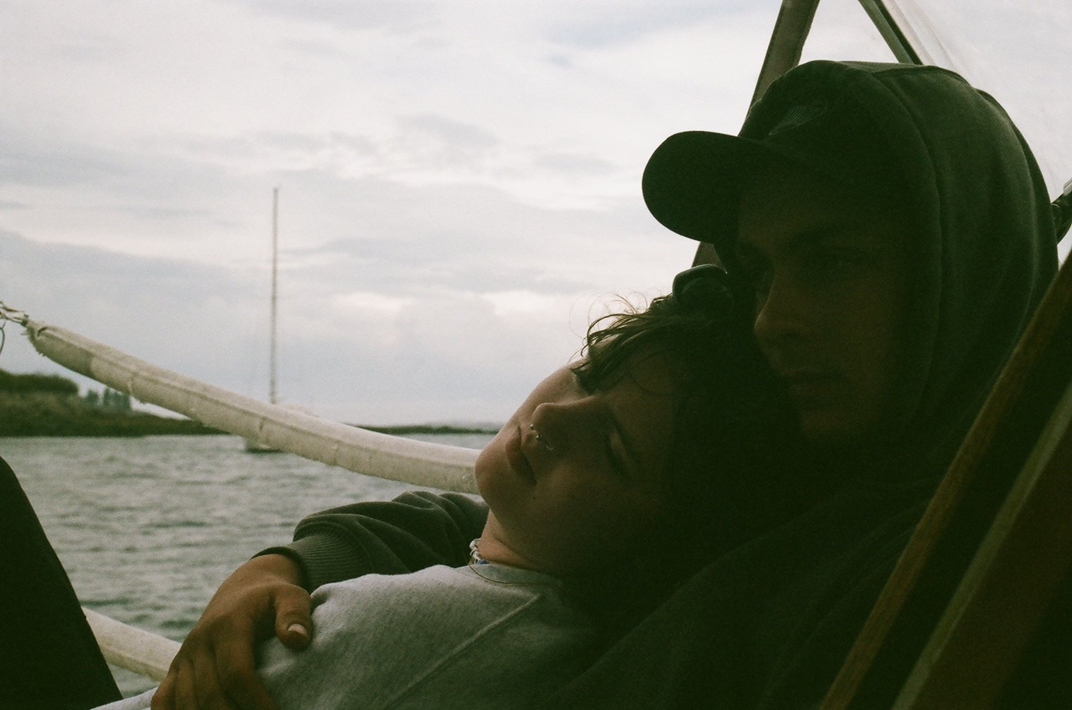 Two people cuddling on a boat, with water and cloudy sky in the background