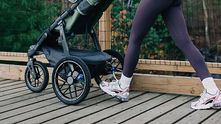 Person stretching on a wooden deck next to a disabled child's stroller with large wheels.