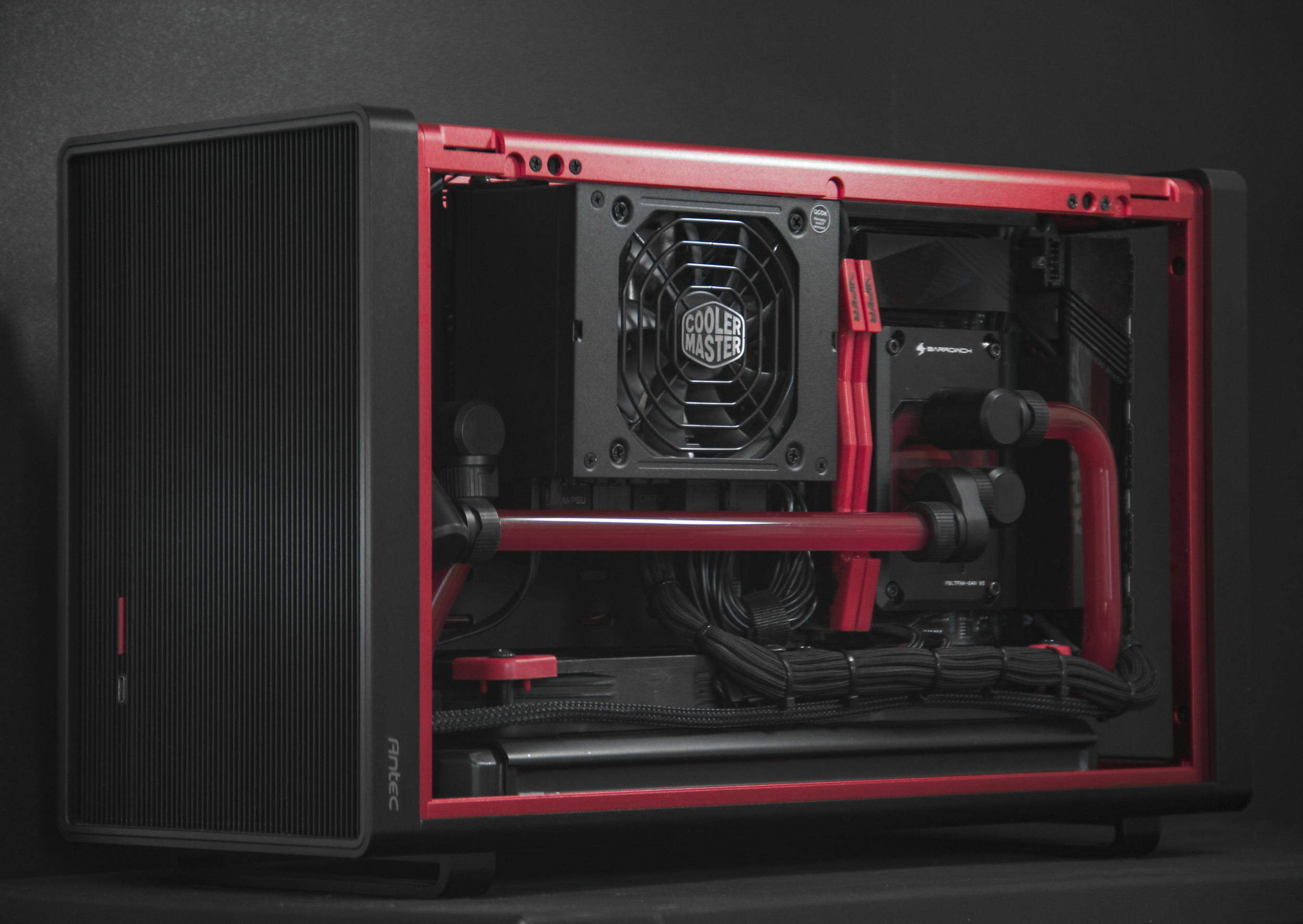 A custom-built computer with a water cooling system, featuring a black case with red accents, a Cooler Master radiator, and red water tubes inside.