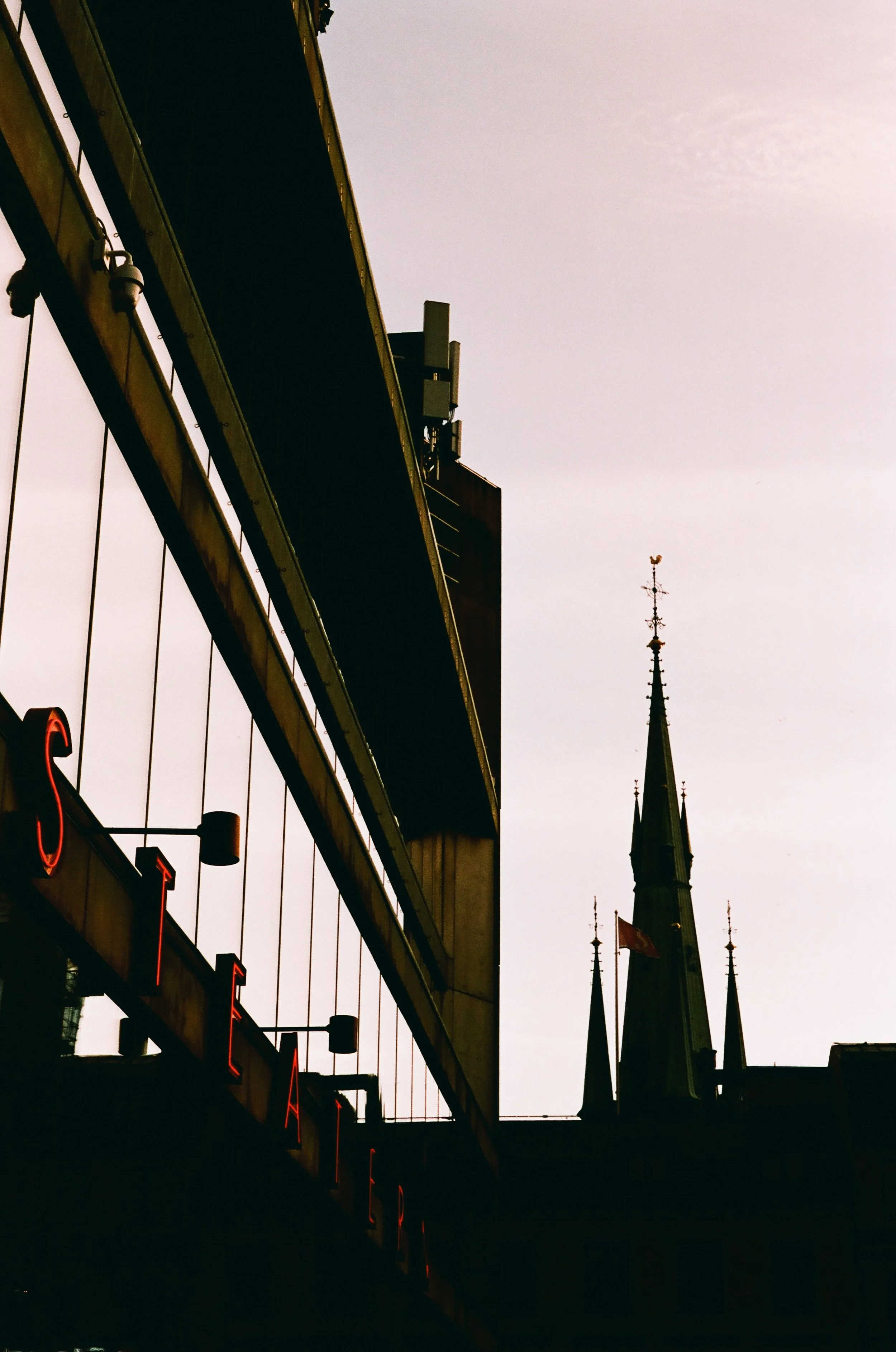 A city street scene with the silhouette of a church steeple and modern buildings, likely in the evening or early morning.