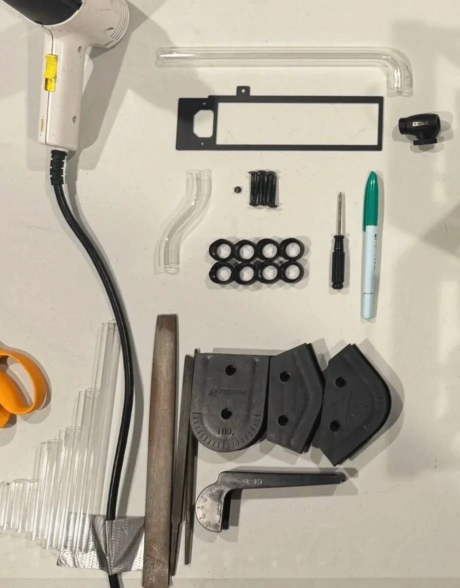 Disassembled components of a 3D printer, including tubing, a heated bed leveling tool, screws, rubber rings, a marker, a screwdriver, and other small parts.
