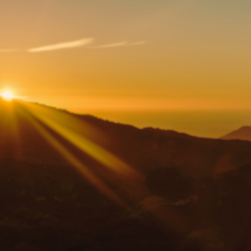 Sunset over mountains with sun rays and a yellow-orange sky.