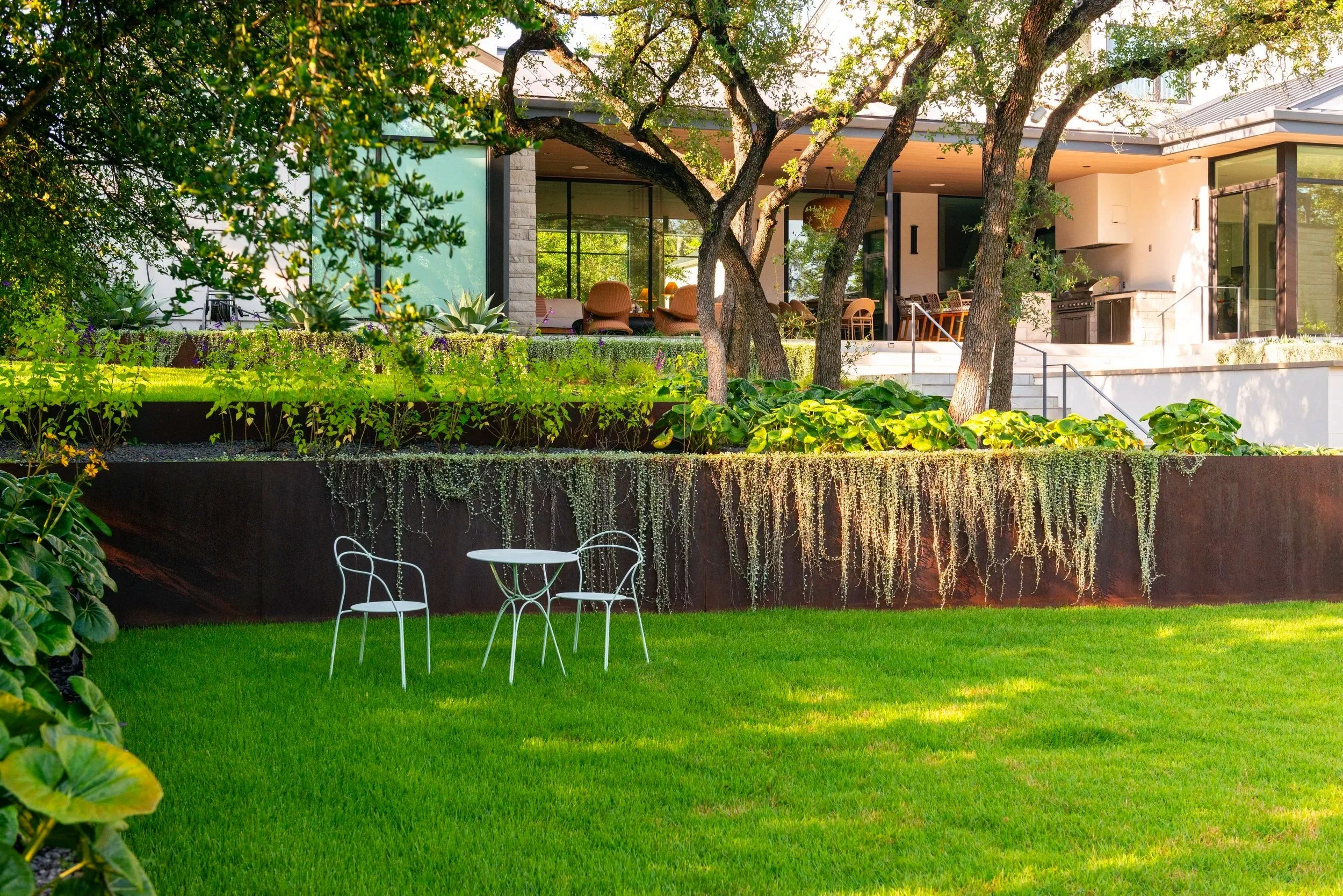 In the backyard, oversized steel terraces create multi-layered tiers of lush planting, defining distinct garden spaces while adding depth, structure, and layers of green.