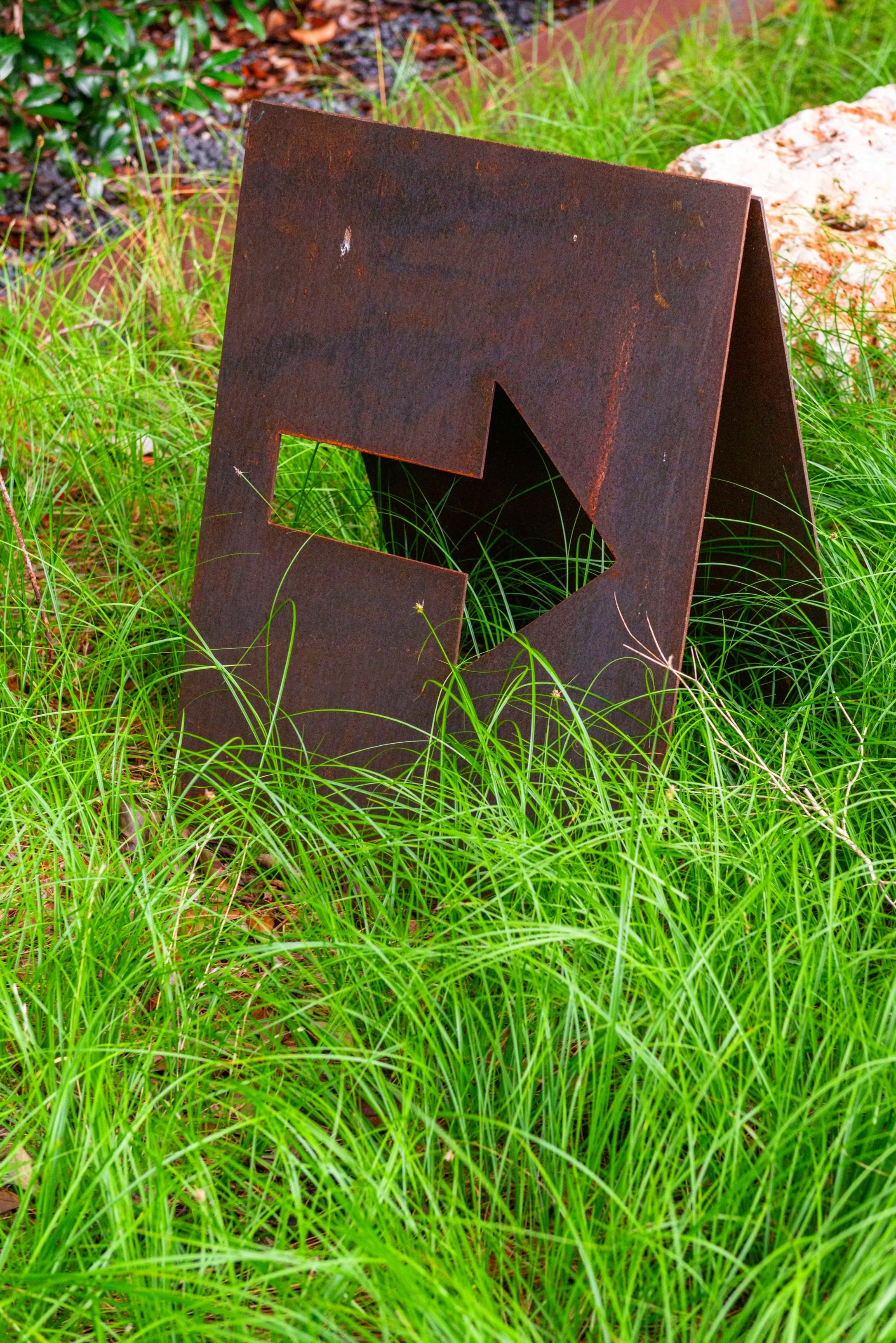 A simple custom steel sign subtly directs visitors toward the path while cleverly concealing ground-level utilities.