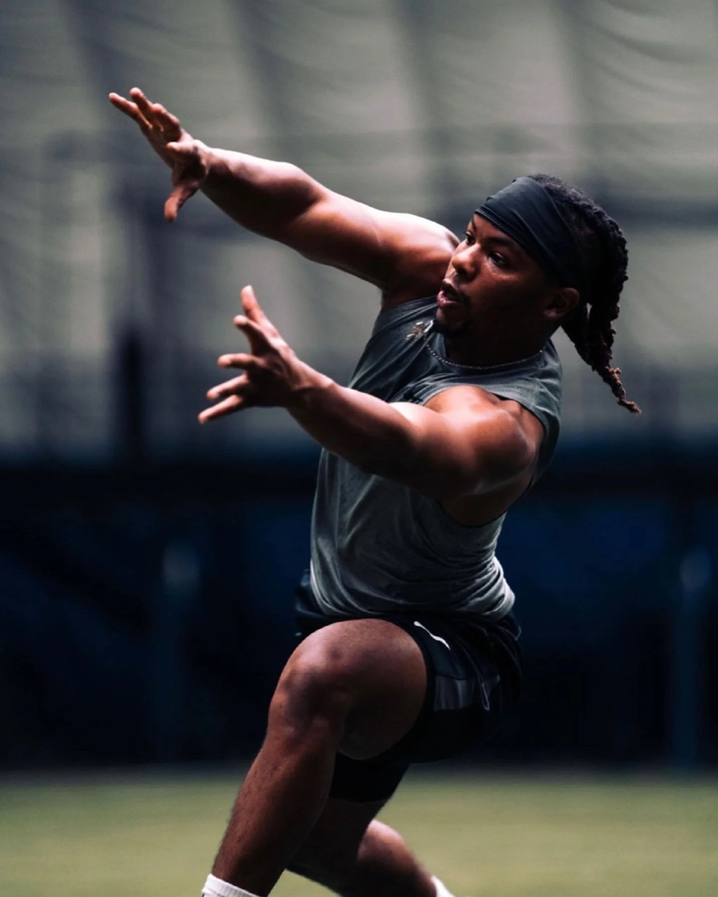 An athlete practicing football drills indoors, wearing a black headband and athletic attire.