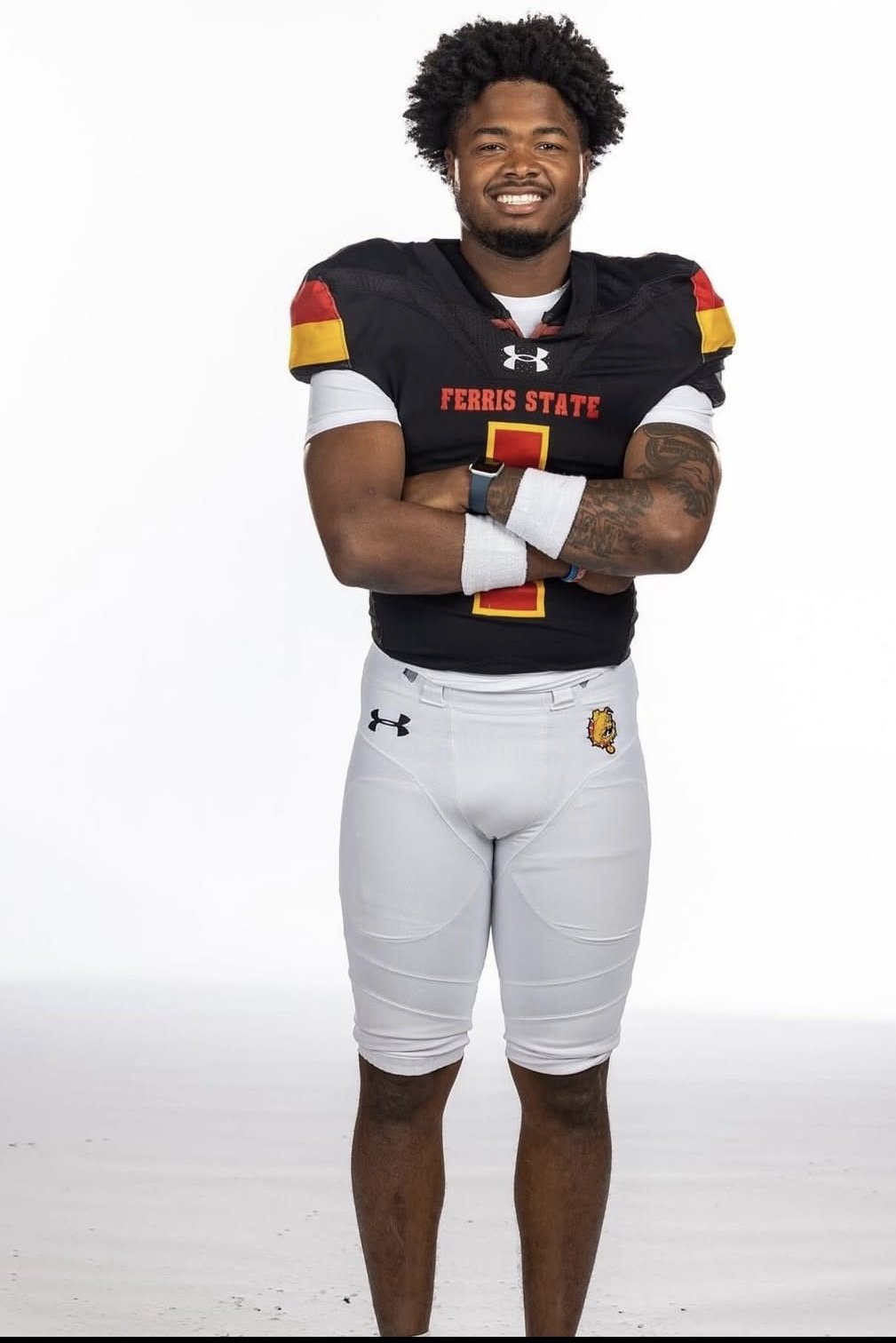 A football player wearing a black and white uniform with red and yellow accents, standing with arms crossed against a plain white background.