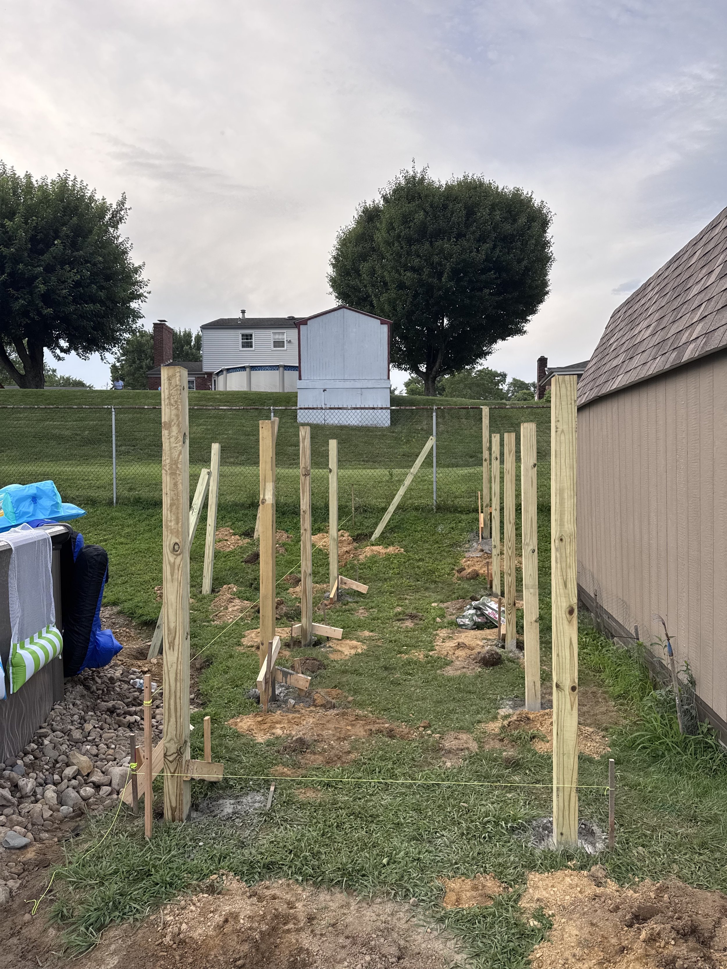 Construction site with wooden posts and strings for a fence or structure in backyard.