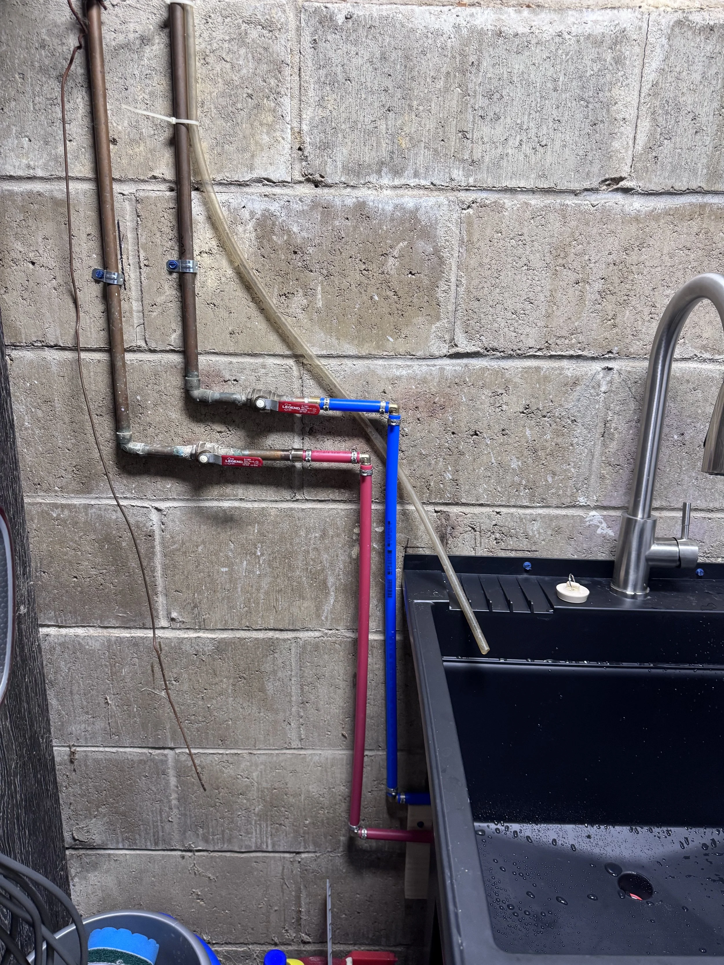 Water supply pipes and a sink in a utility room or garage with a concrete wall background.