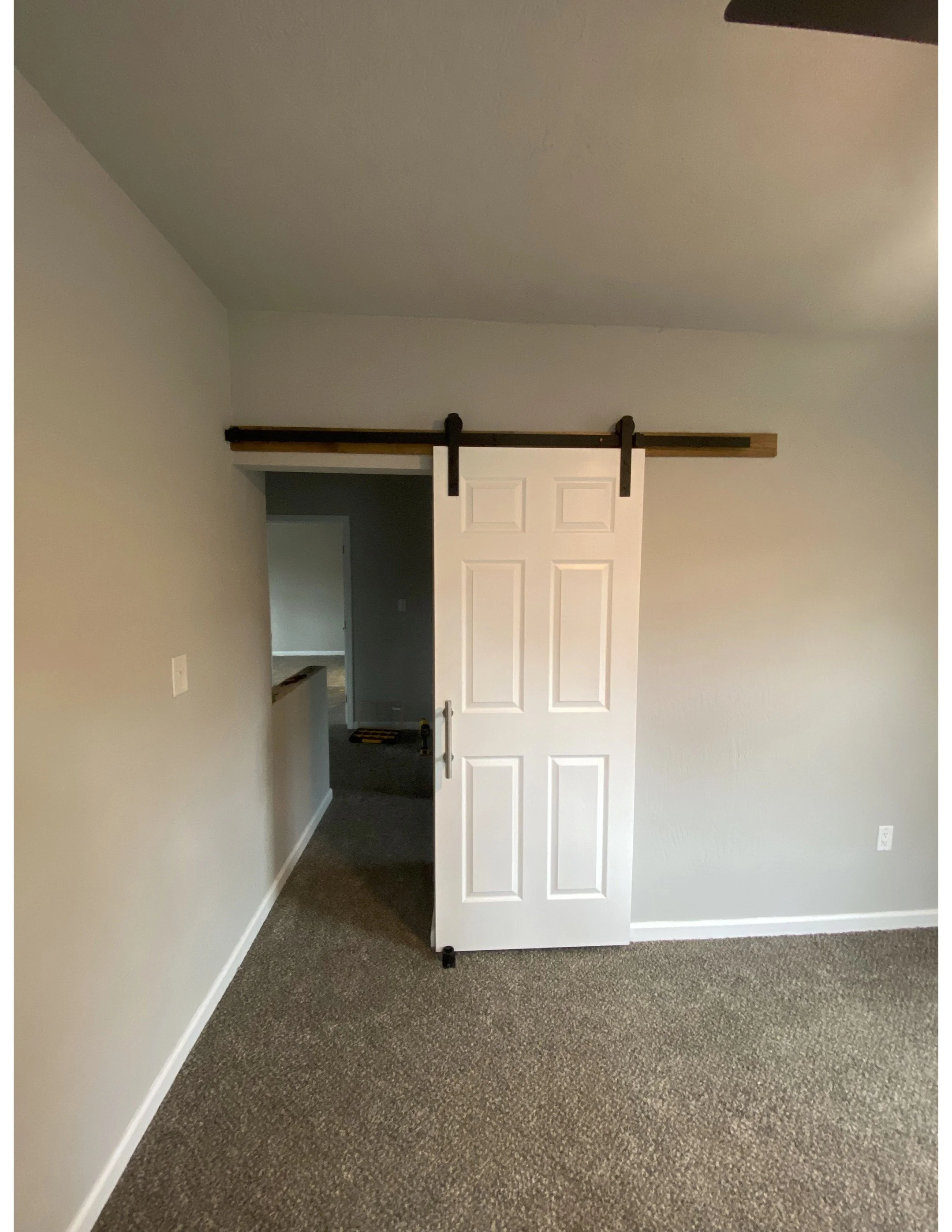 Interior view of a room with gray walls, brown carpet, a white door on a wooden sliding barn door track.