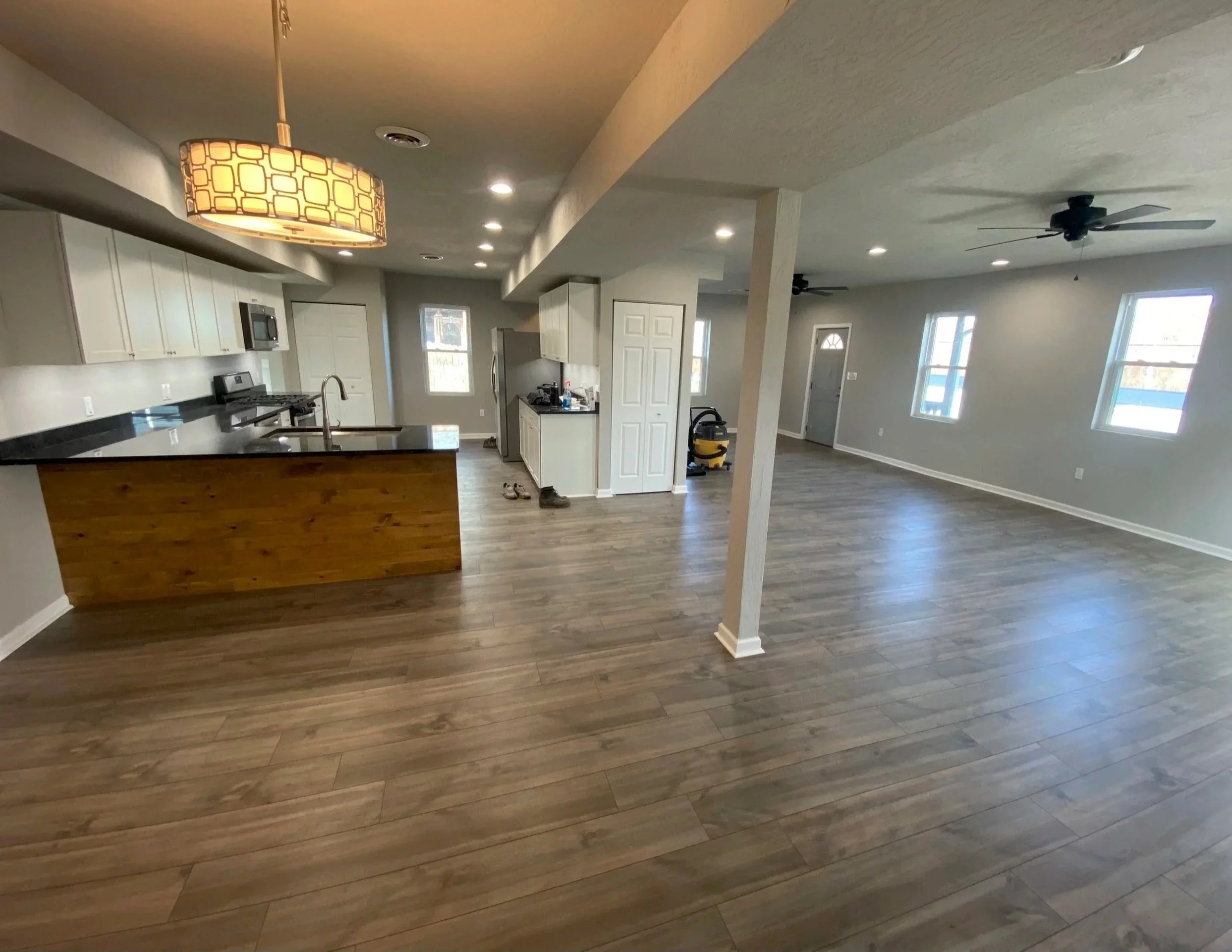 Open-concept living space with hardwood floors, a kitchen with white cabinets, black countertops, stainless steel appliances, and a dining area with a large ceiling light fixture.