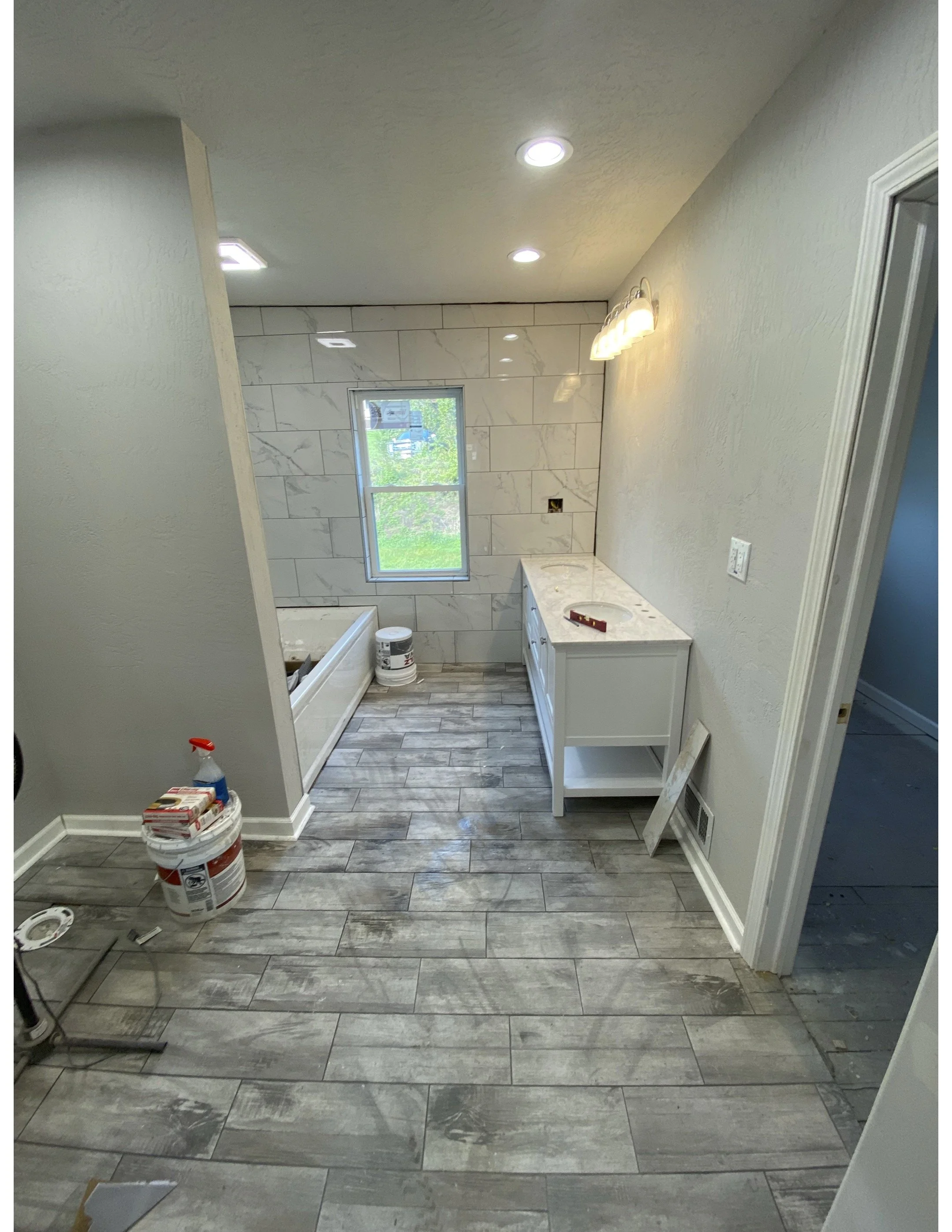 Bathroom under construction with gray wood-look tile flooring, partial wall with white marble tiles, a window, and a white vanity