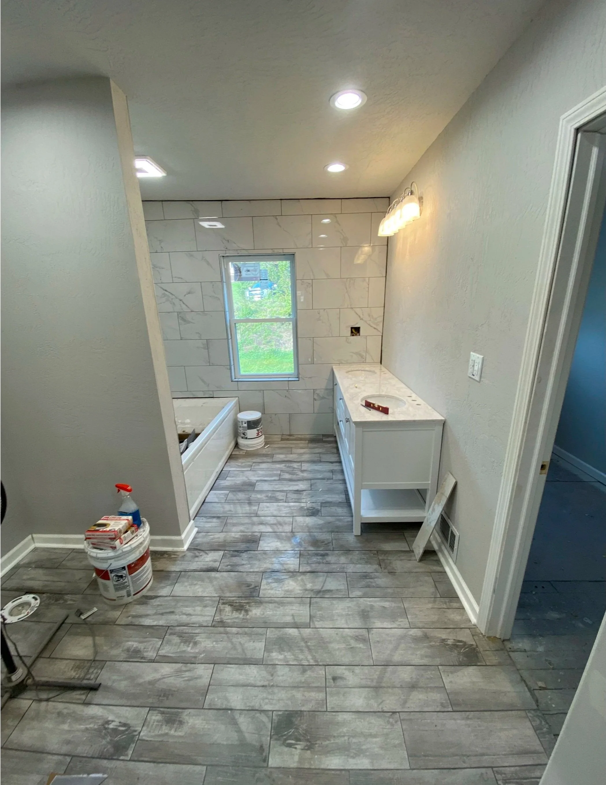 Bathroom under renovation with a bathtub, a window, a vanity, and renovation supplies on the floor.