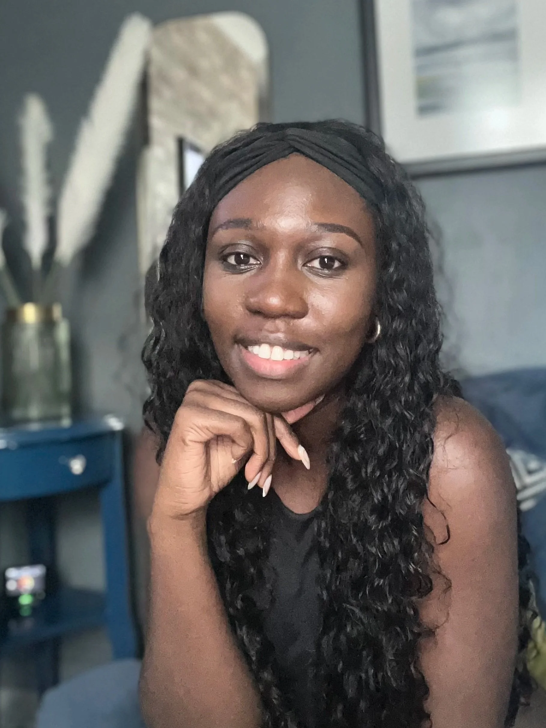 Dr Alria Williams with curly black hair, smiling and resting her chin on her hand in a cozy indoor setting.