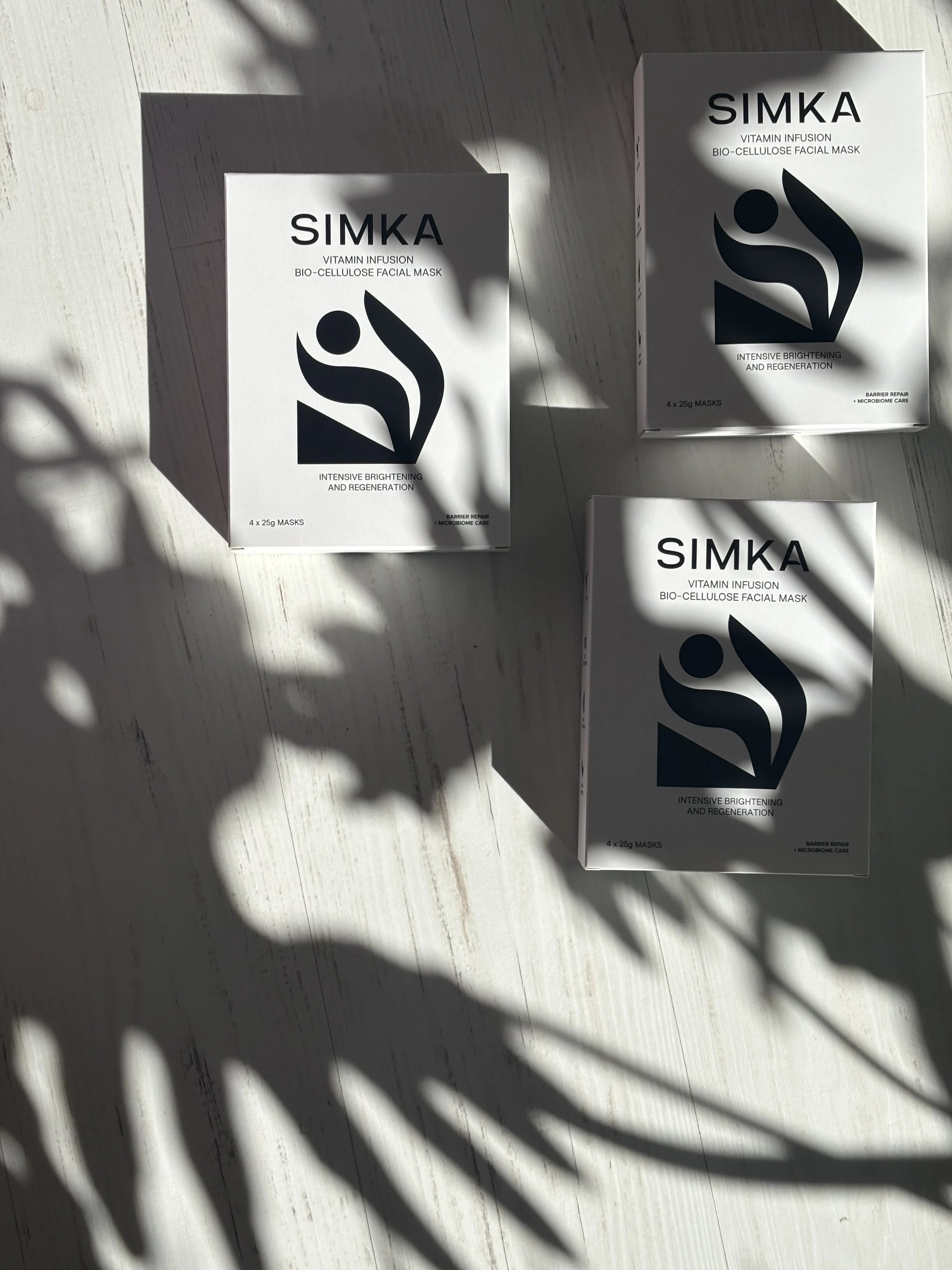 Three boxes of SIMKA vitamin infusion bio-cellulose facial masks on a light wooden surface with shadows.