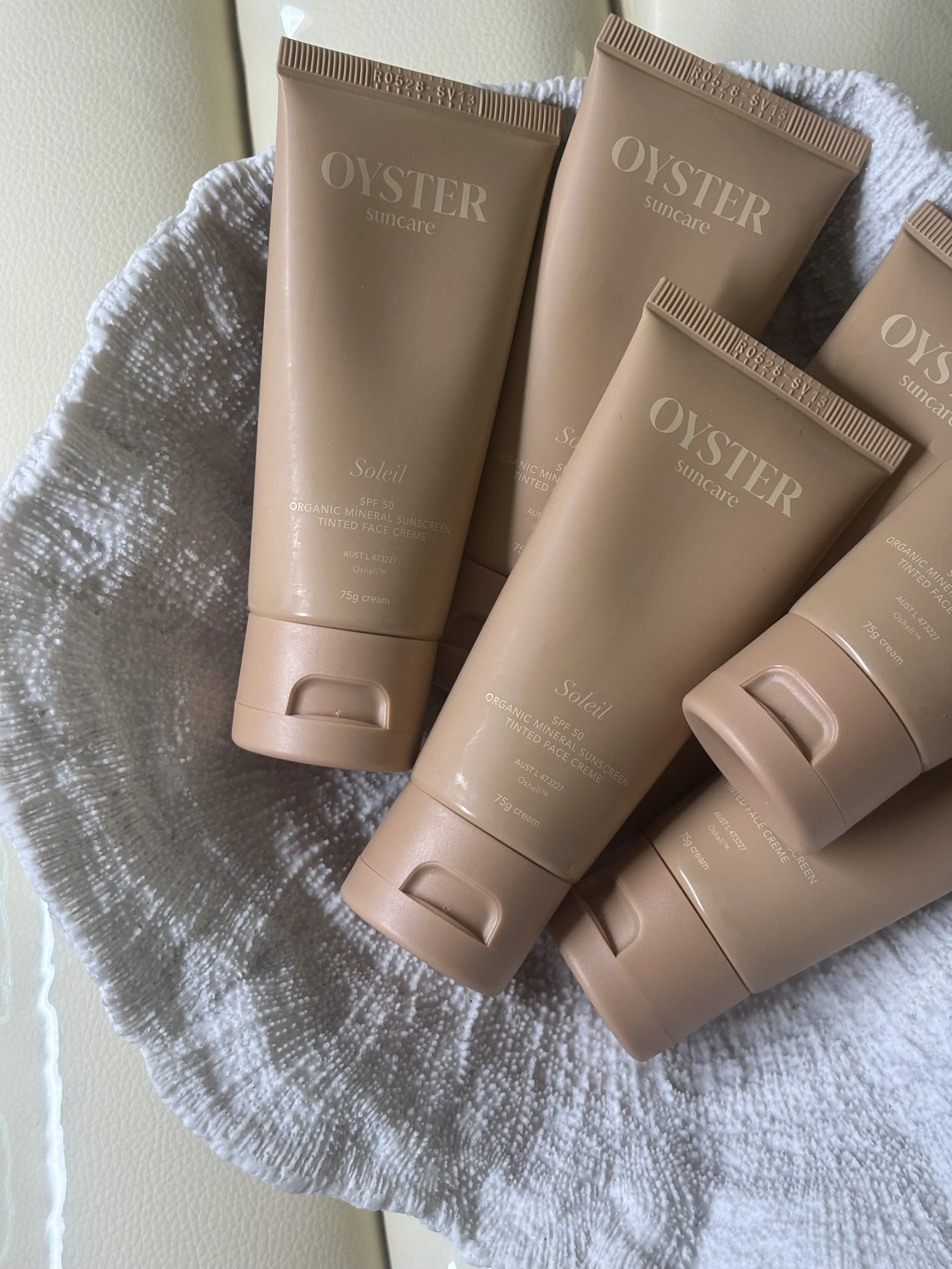 Multiple tubes of Oyster Suncare SPF 50 organic mineral sunscreen tinted face cream on a white textured surface.