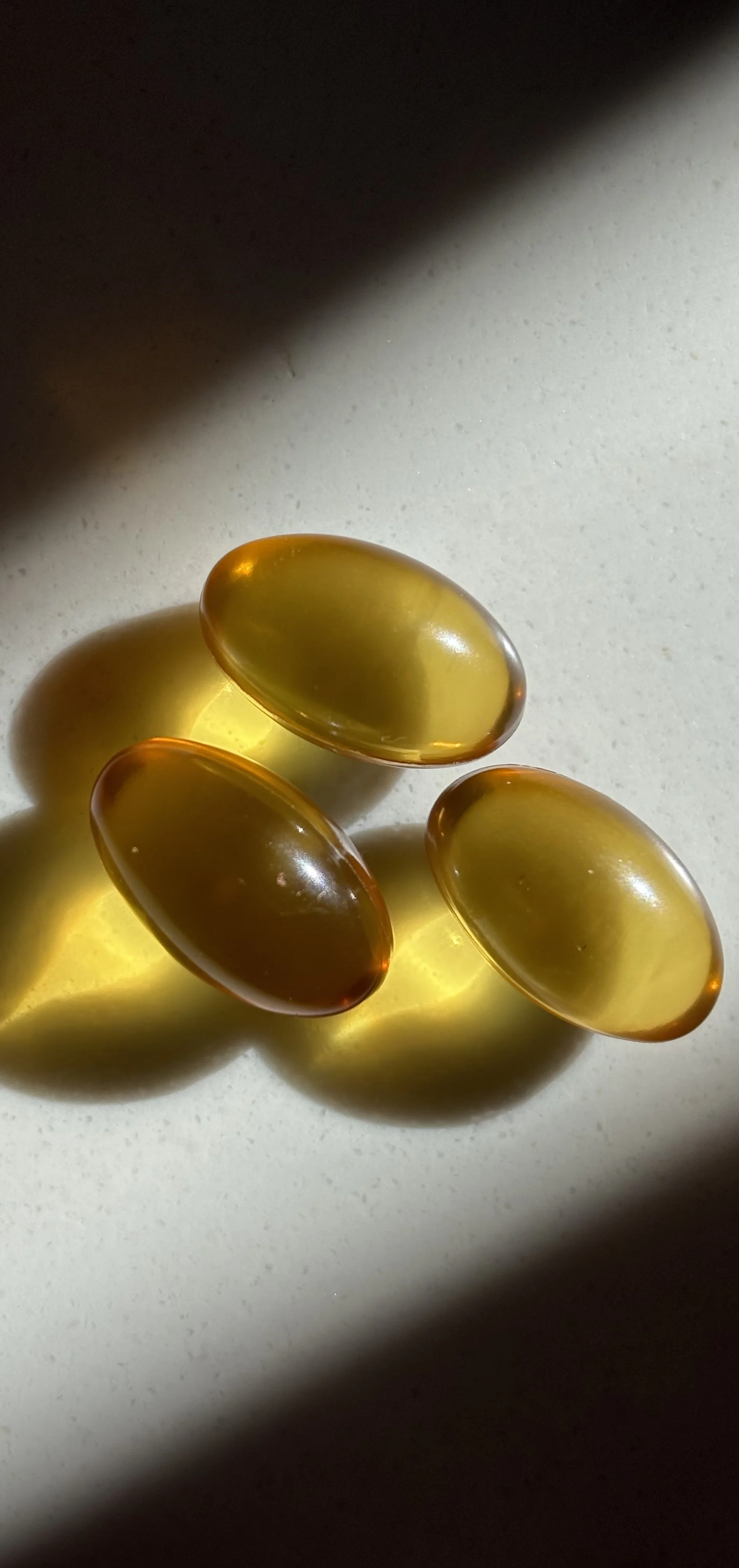 Close-up of four yellowish translucent capsules on a white surface with shadows cast by the capsules.