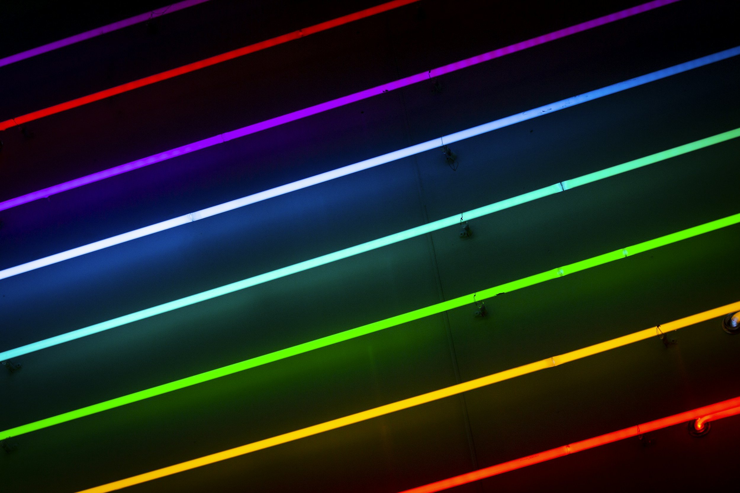 Multiple horizontal neon light strips in various colors, including purple, red, blue, green, yellow, and orange, attached to a dark ceiling.