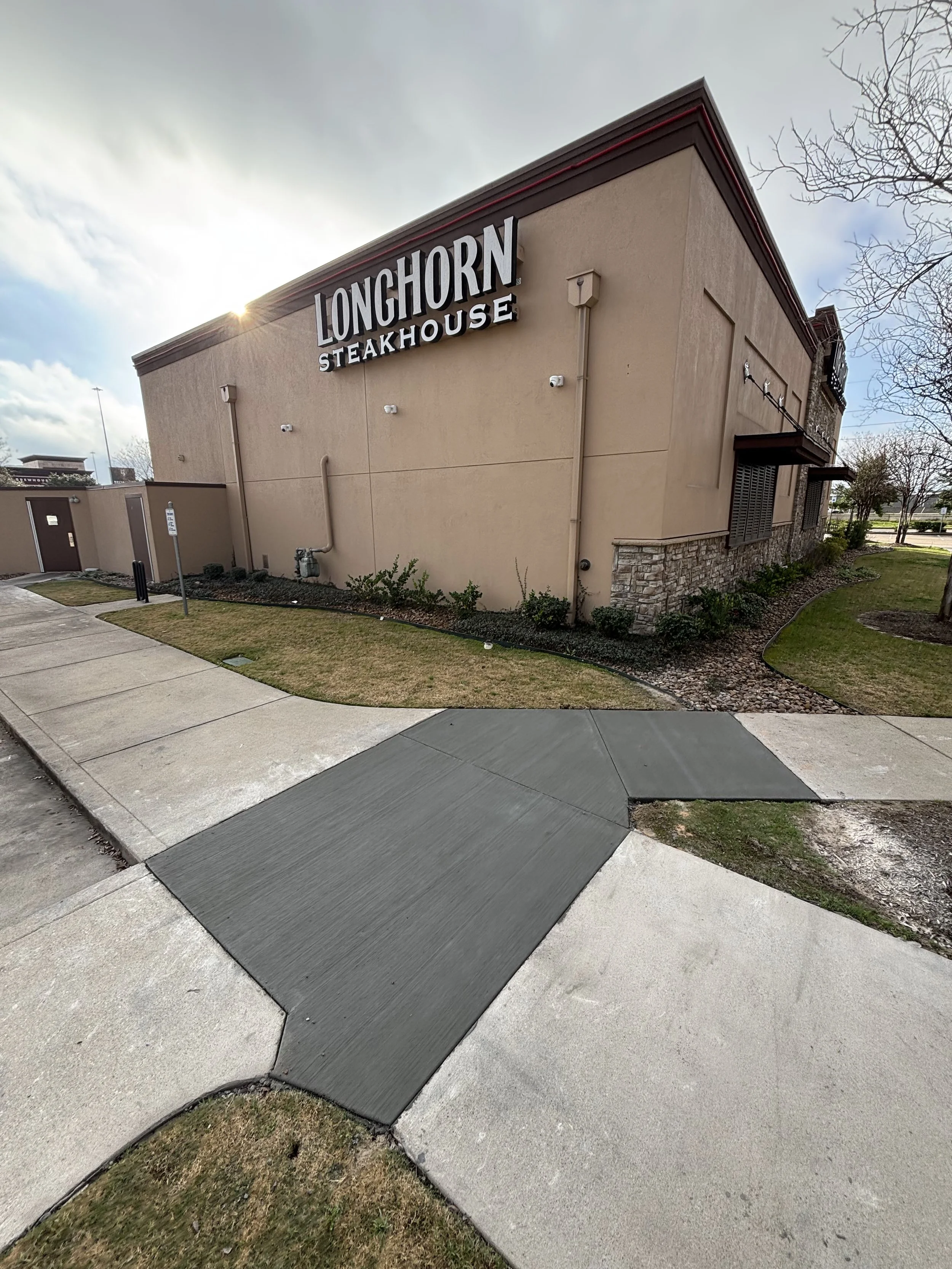 LongHorn Steakhouse building with a sidewalk ramp in the foreground and clear sky in the background.