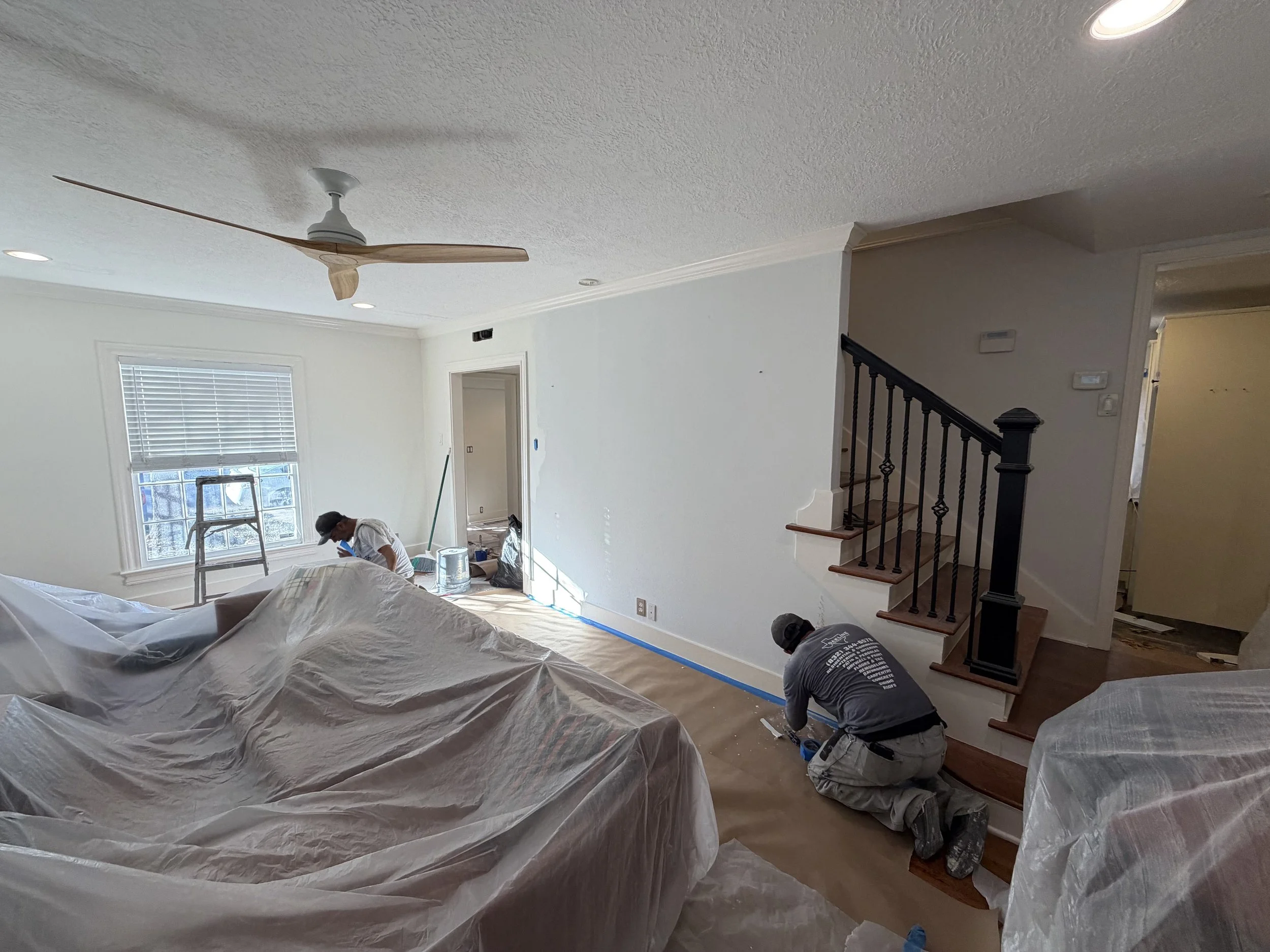 Two workers painting a staircase in a living room during renovation.