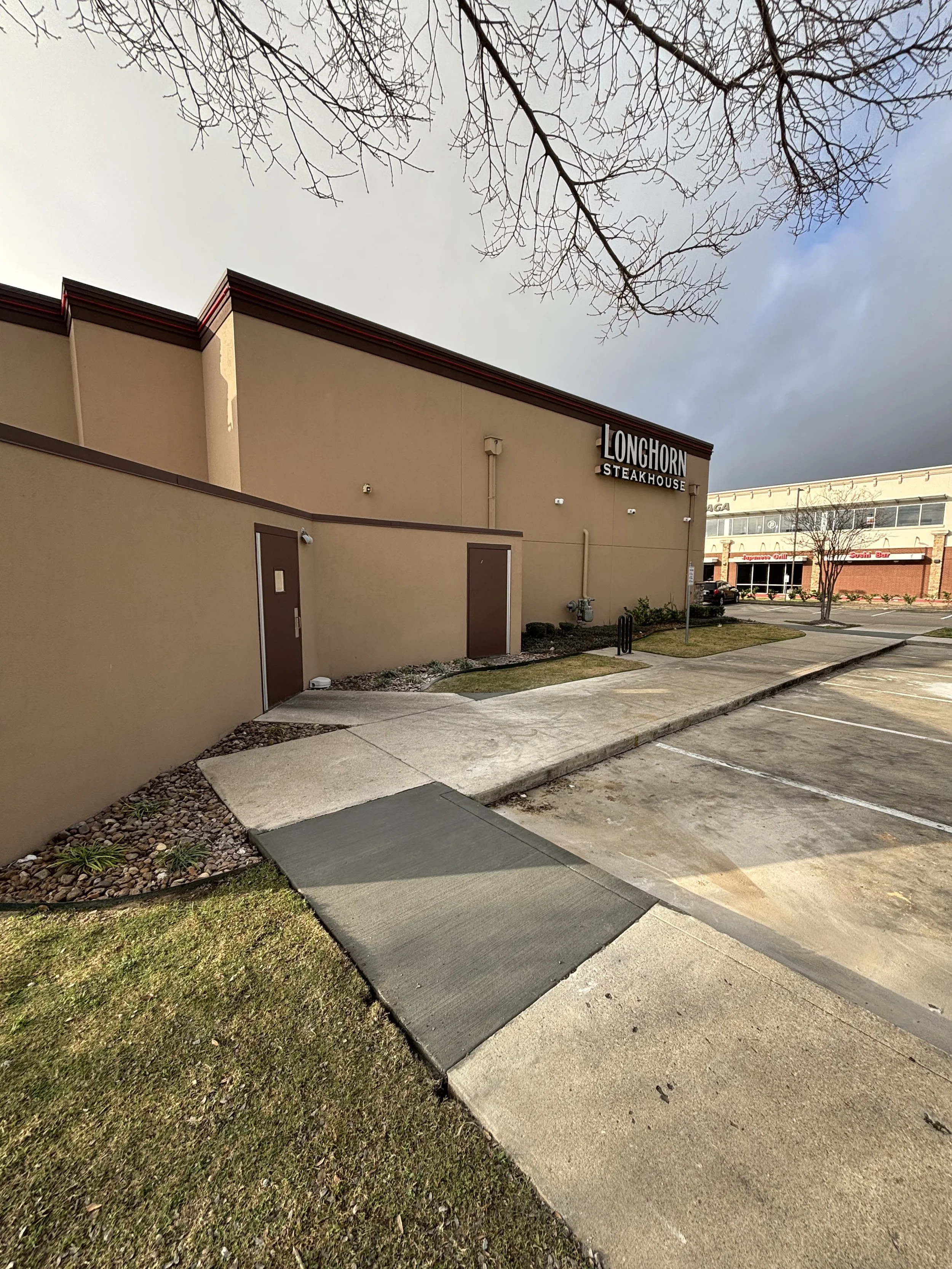 Exterior view of Longhorn Steakhouse restaurant with parking lot, sidewalk, and leafless tree branches overhead.