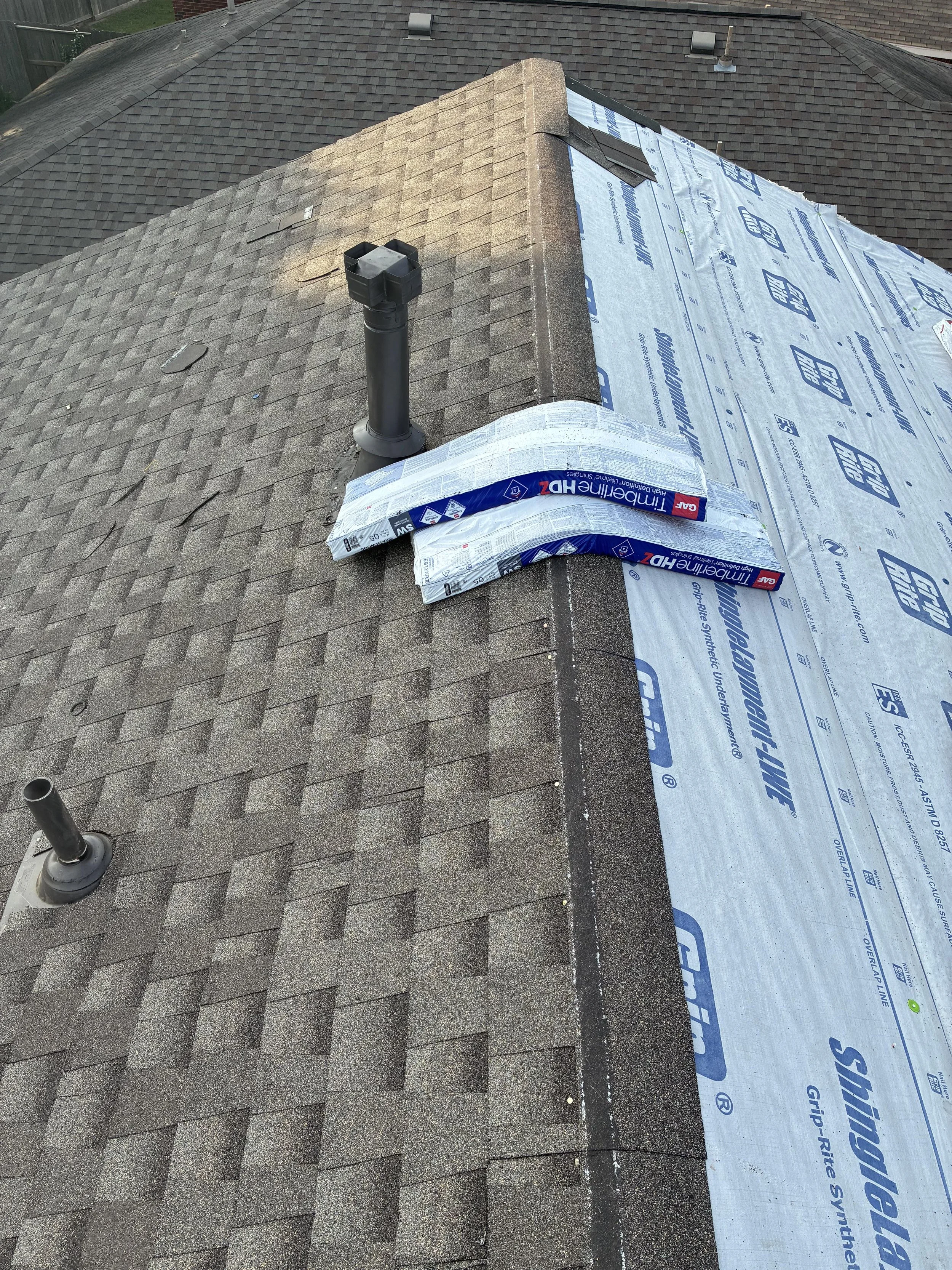 Roof with new Underlayment and vent pipes, showing shingles and a ridge with partial new flashing.