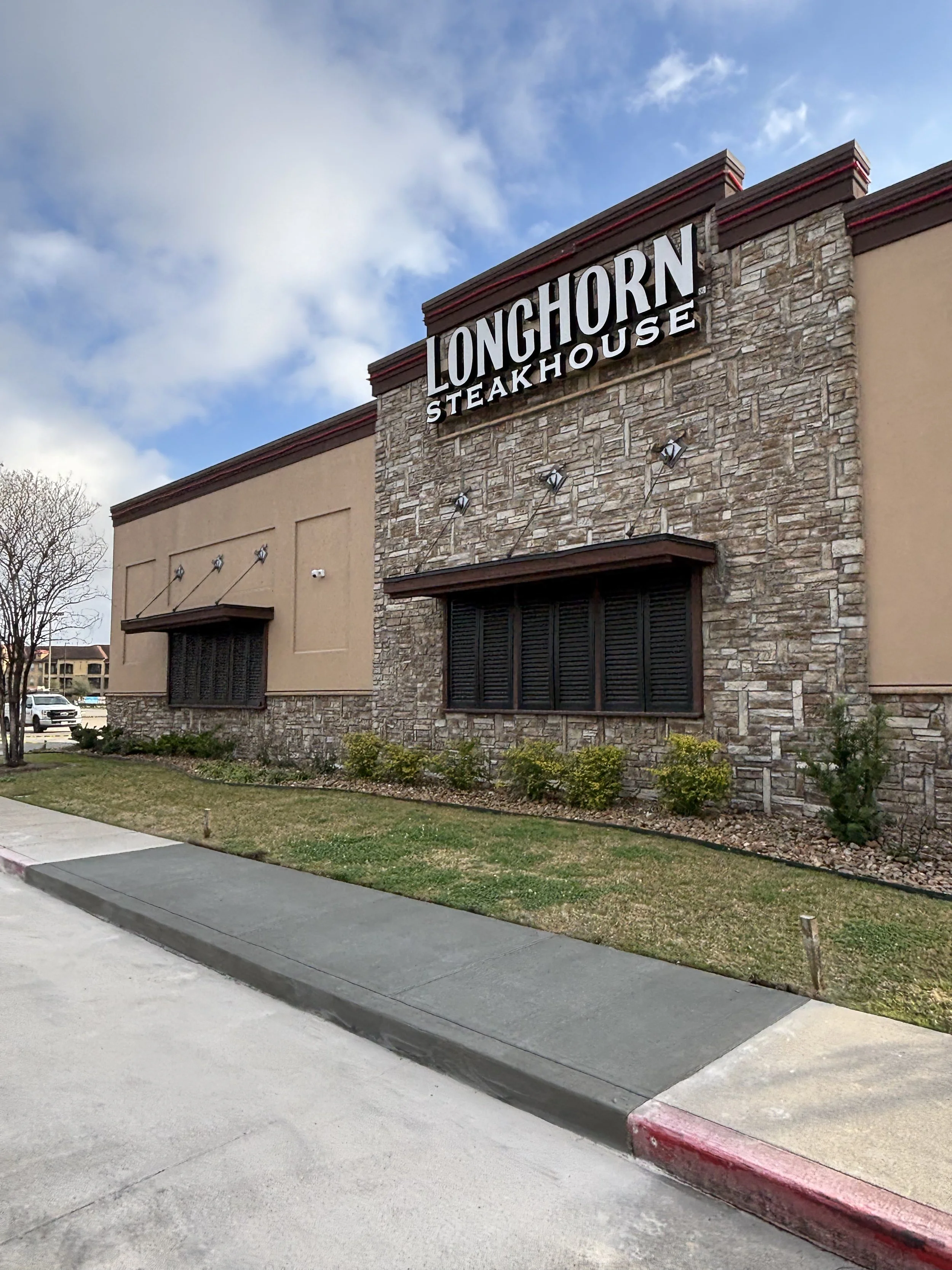 LongHorn Steakhouse restaurant exterior with stone and stucco facade, sign, windows with shutters, and landscaped yard.