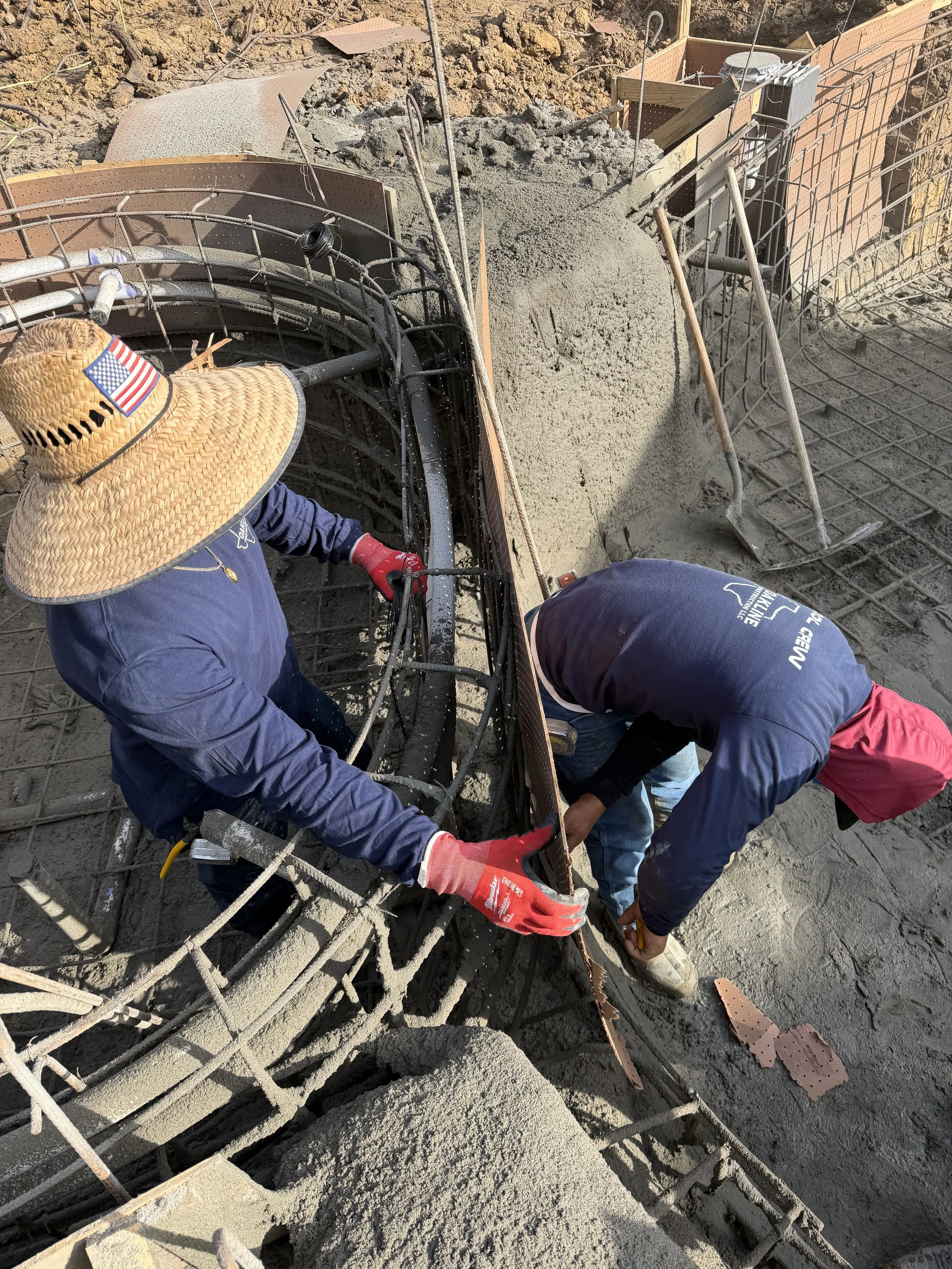 Two construction workers working on a rebar structure at a construction site, pouring and shaping concrete.