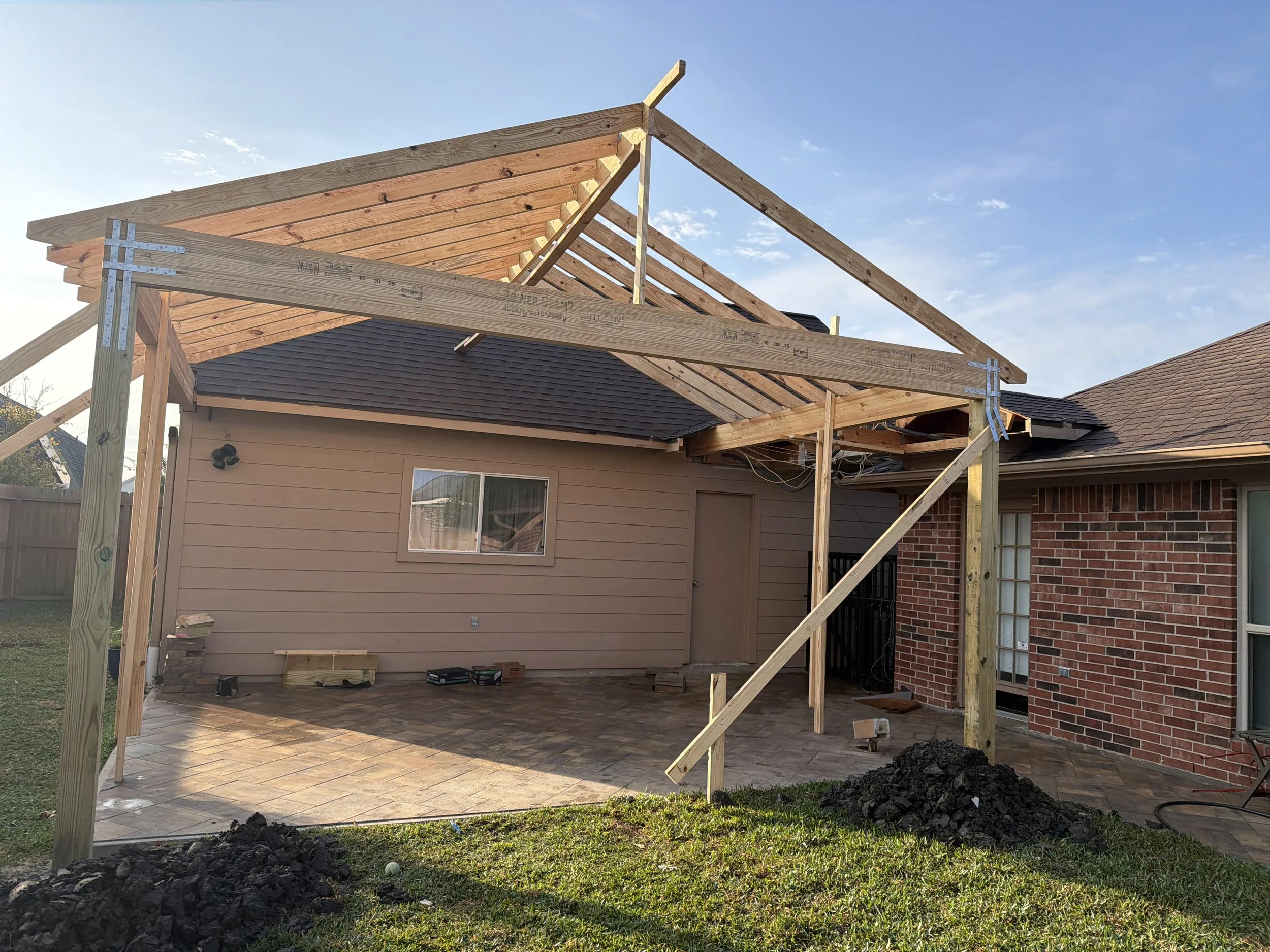Construction of a new porch with wooden framing in a backyard, with tools and dirt piles nearby.
