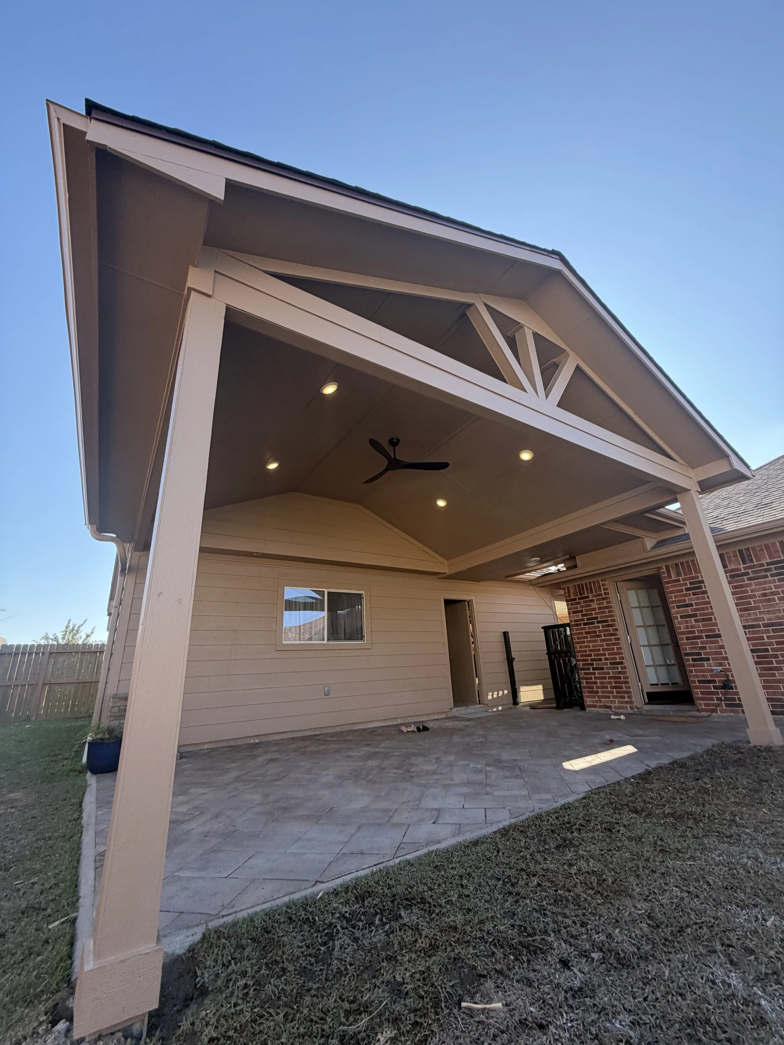 Backyard patio area with a covered porch, ceiling fan, ceiling lights, sliding glass door, window, and brick wall.