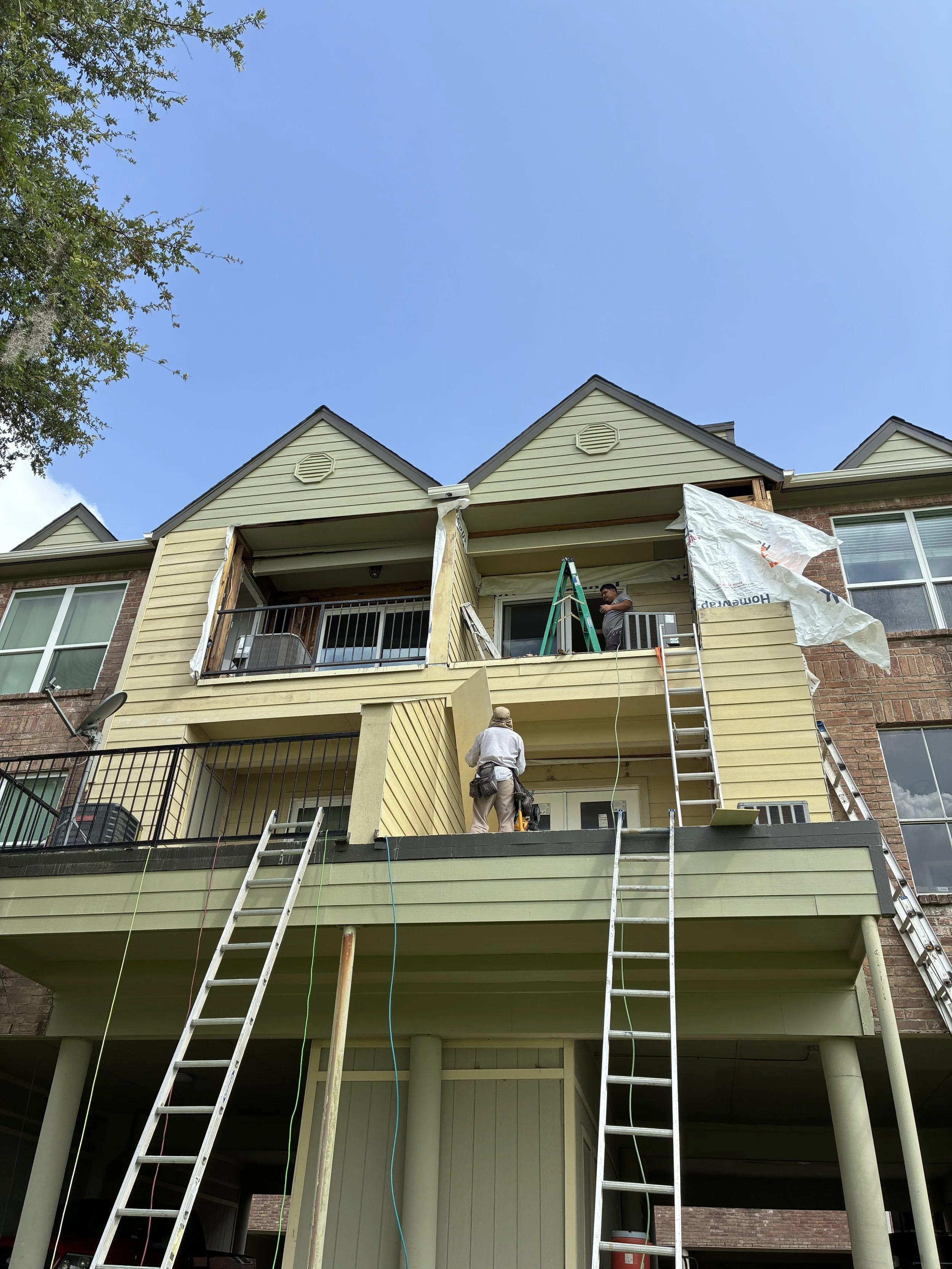 Construction workers renovating the outside of a multi-story building, with ladders and tools, during daytime.