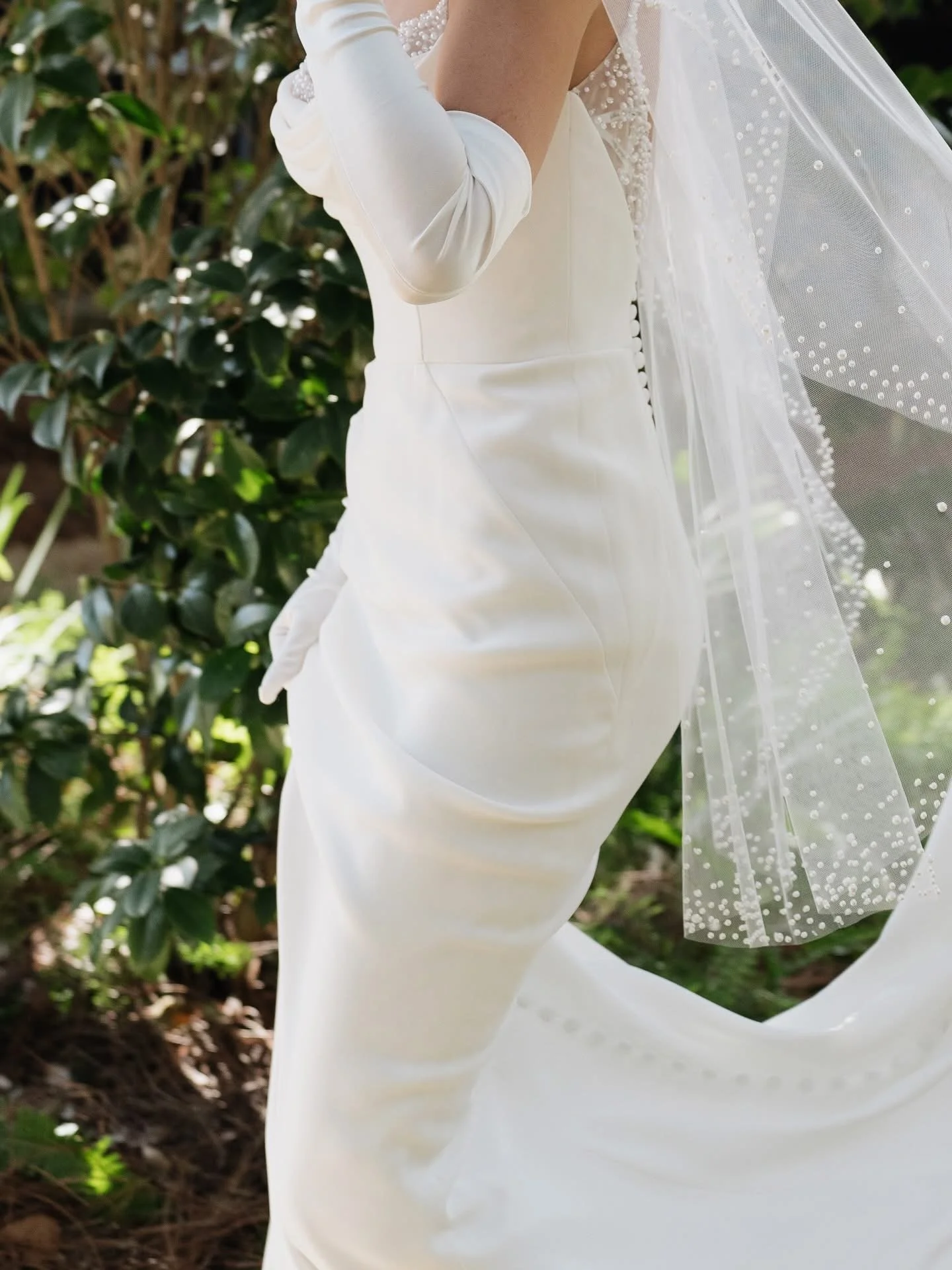 Close-up of a person wearing a white wedding dress with gloves and veil outdoors.