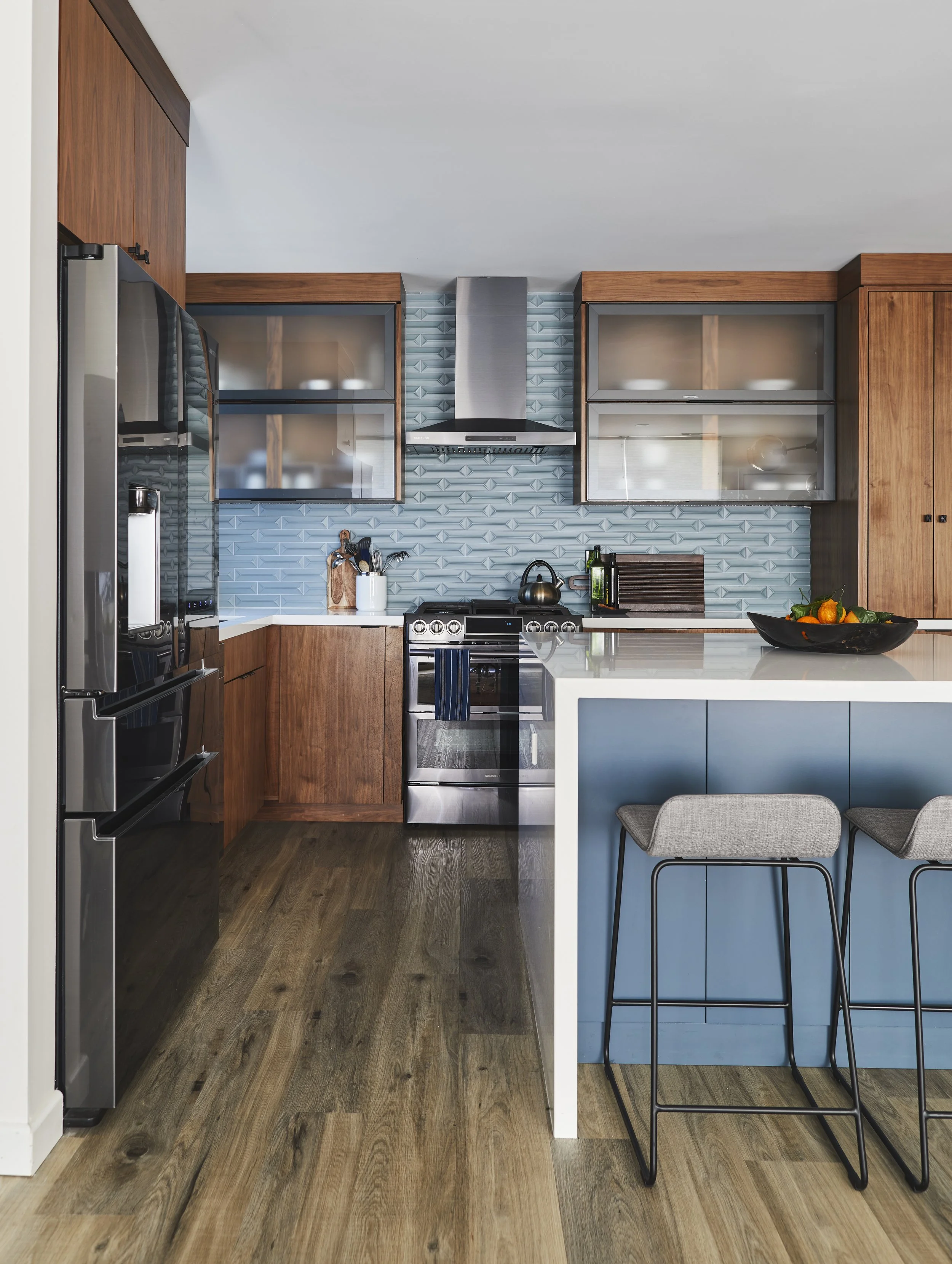 Modern kitchen with wooden cabinets, stainless steel appliances, a blue tile backsplash, and an island with bar stools.