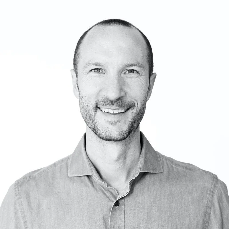 Black and white portrait of a smiling man with short hair, a beard, wearing a collared shirt, against a plain background.