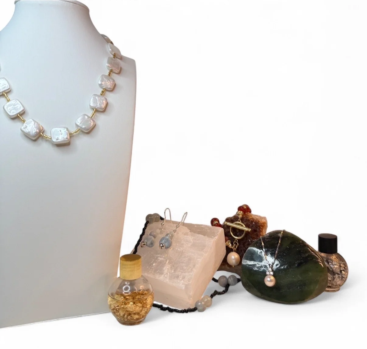 Jewelry display with necklaces, earrings, and rings arranged on a white background, featuring pearls, beads, and stones.