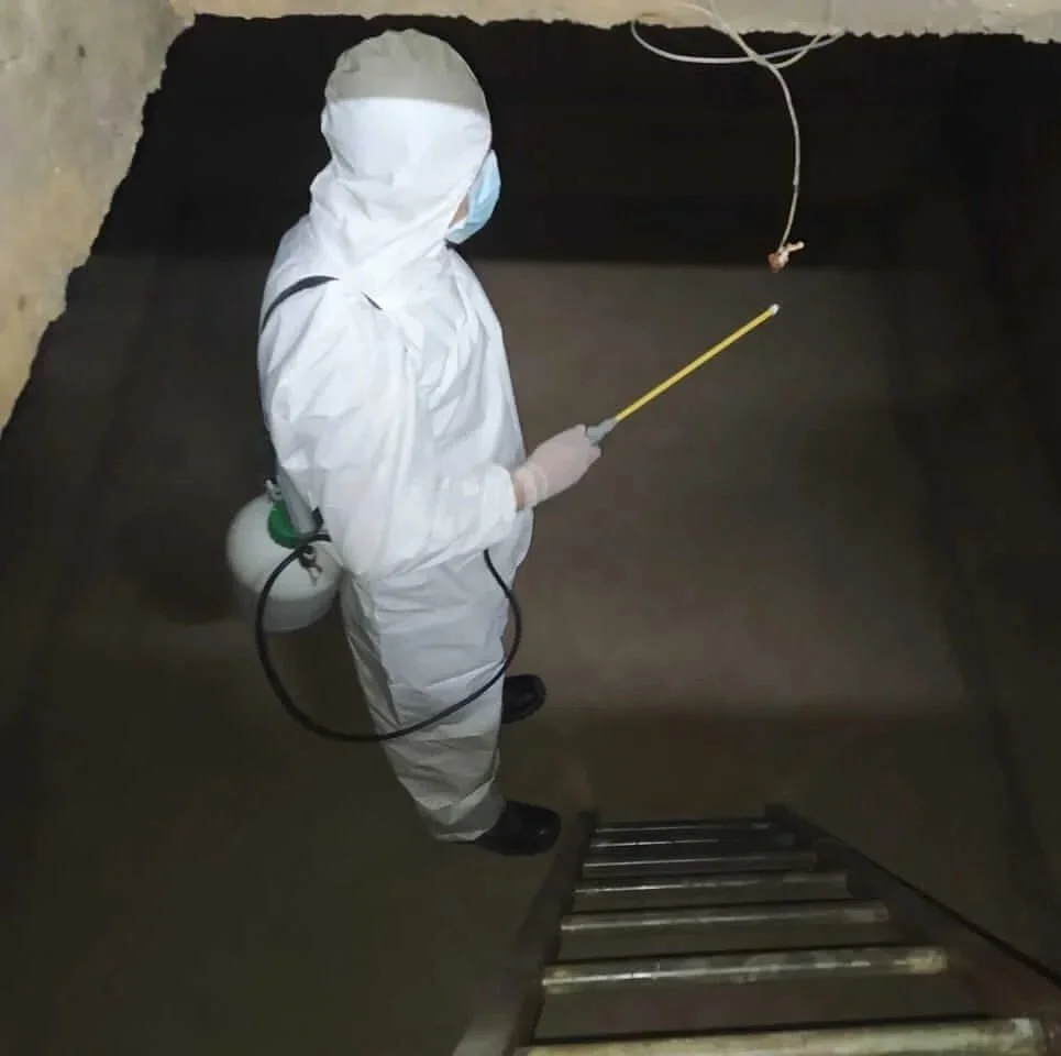 Persona con ropa protectora y mascarilla desinfectando una piscina de agua.