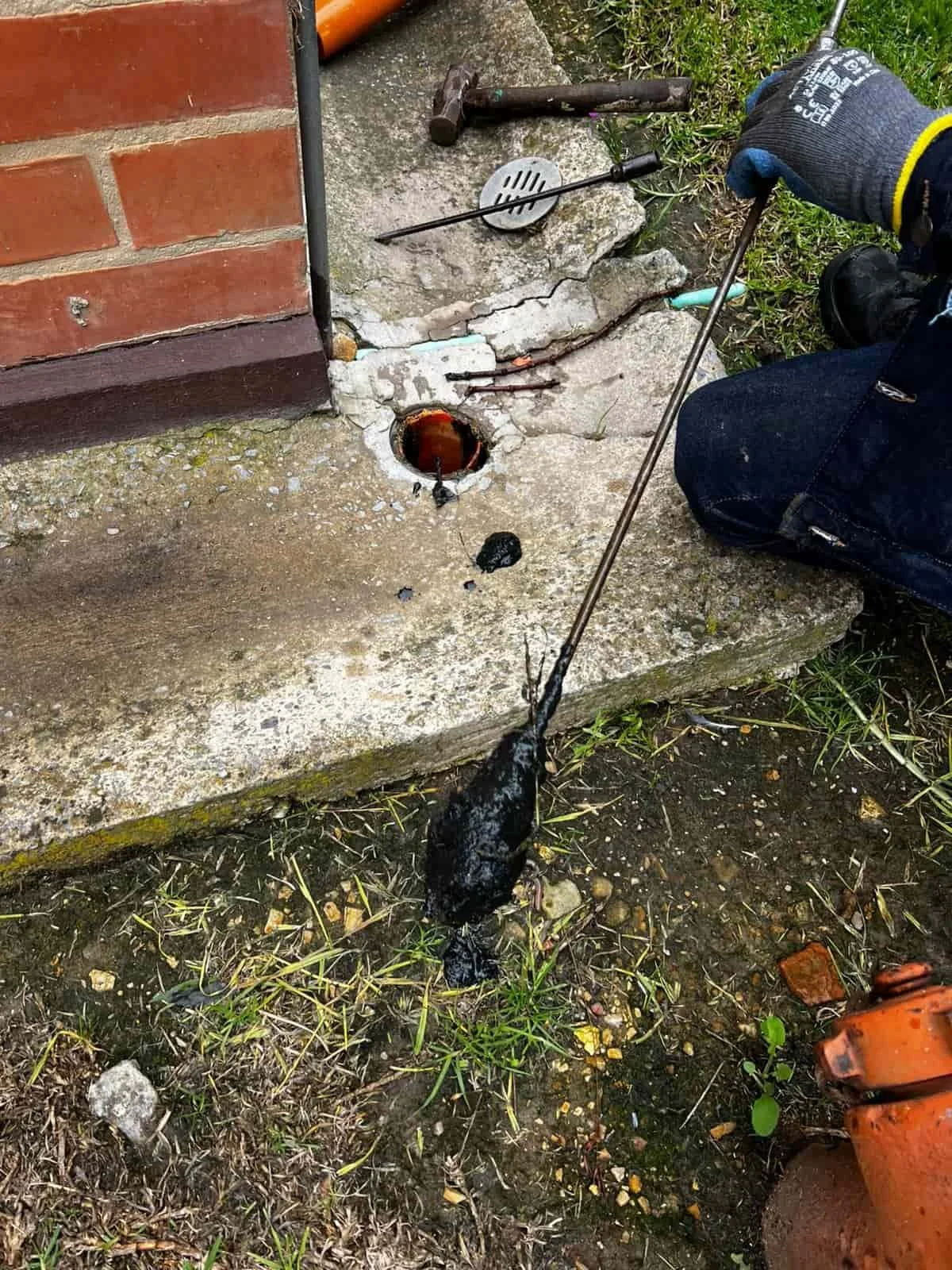 Técnico trabajando en una reparación de plomería en la tubería que sale de la casa, con herramientas y guantes.