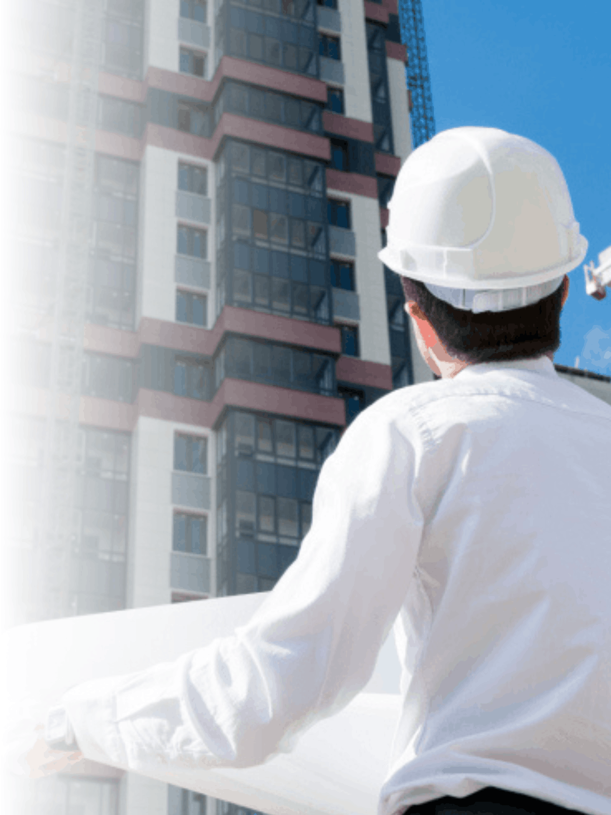 Un ingeniero con casco y ropa blanca inspecciona un edificio en construcción en un día soleado.