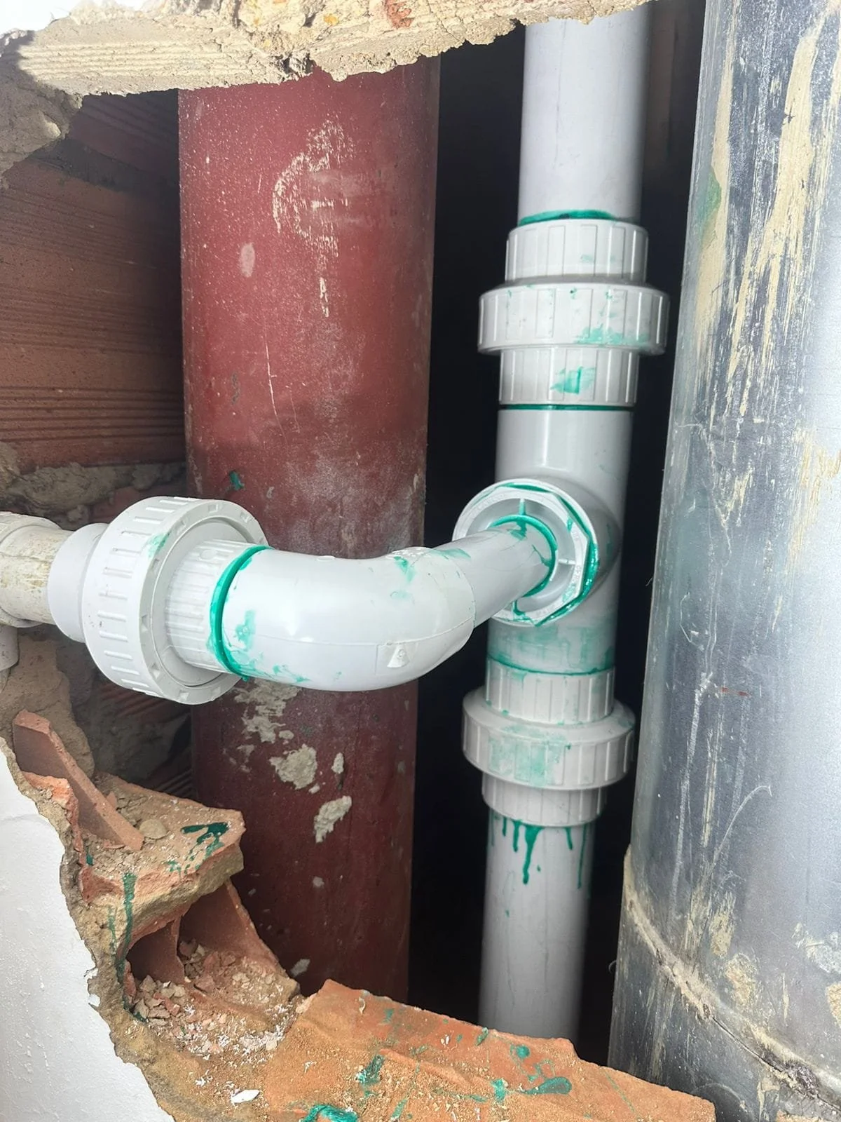 Válvula de plástico y tuberías en una construcción, con pintura verde y partes de cerámica enrosadas.