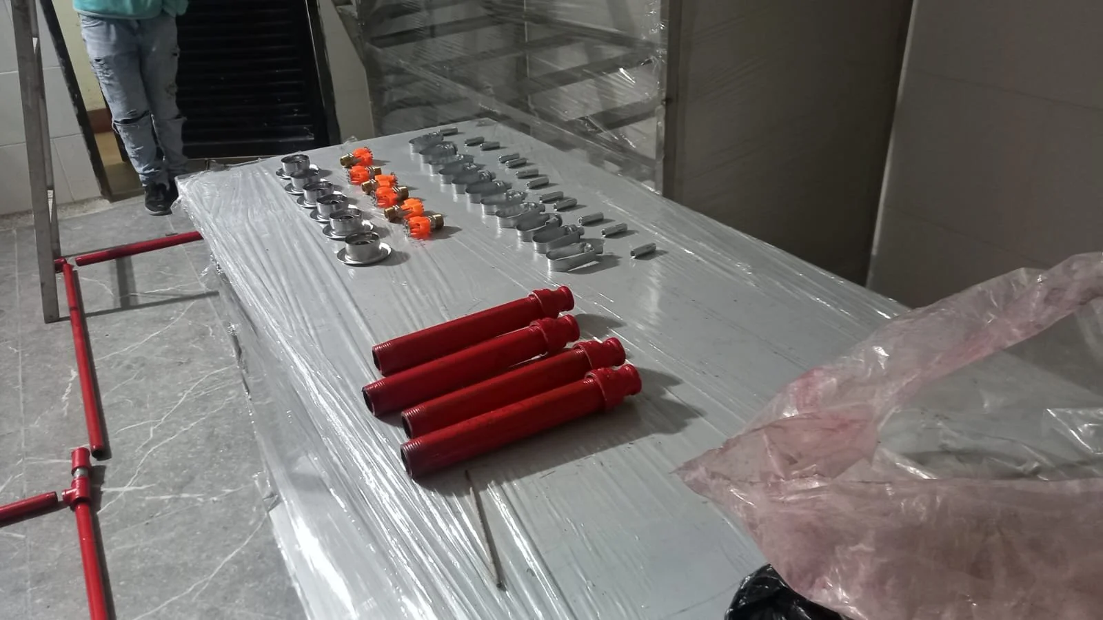 Herramientas y piezas metálicas colocadas sobre una mesa de trabajo cubierta con plástico en un ambiente industrial.