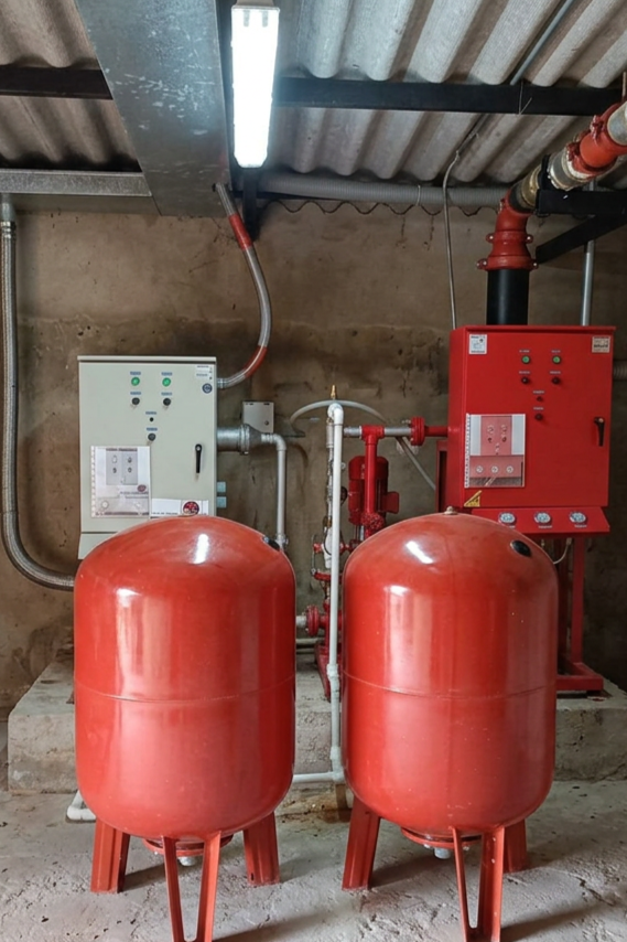 Sistema de control de incendios con dos cilindros rojos grandes, un panel de control y tuberías conectadas en un cuarto de maquinas.