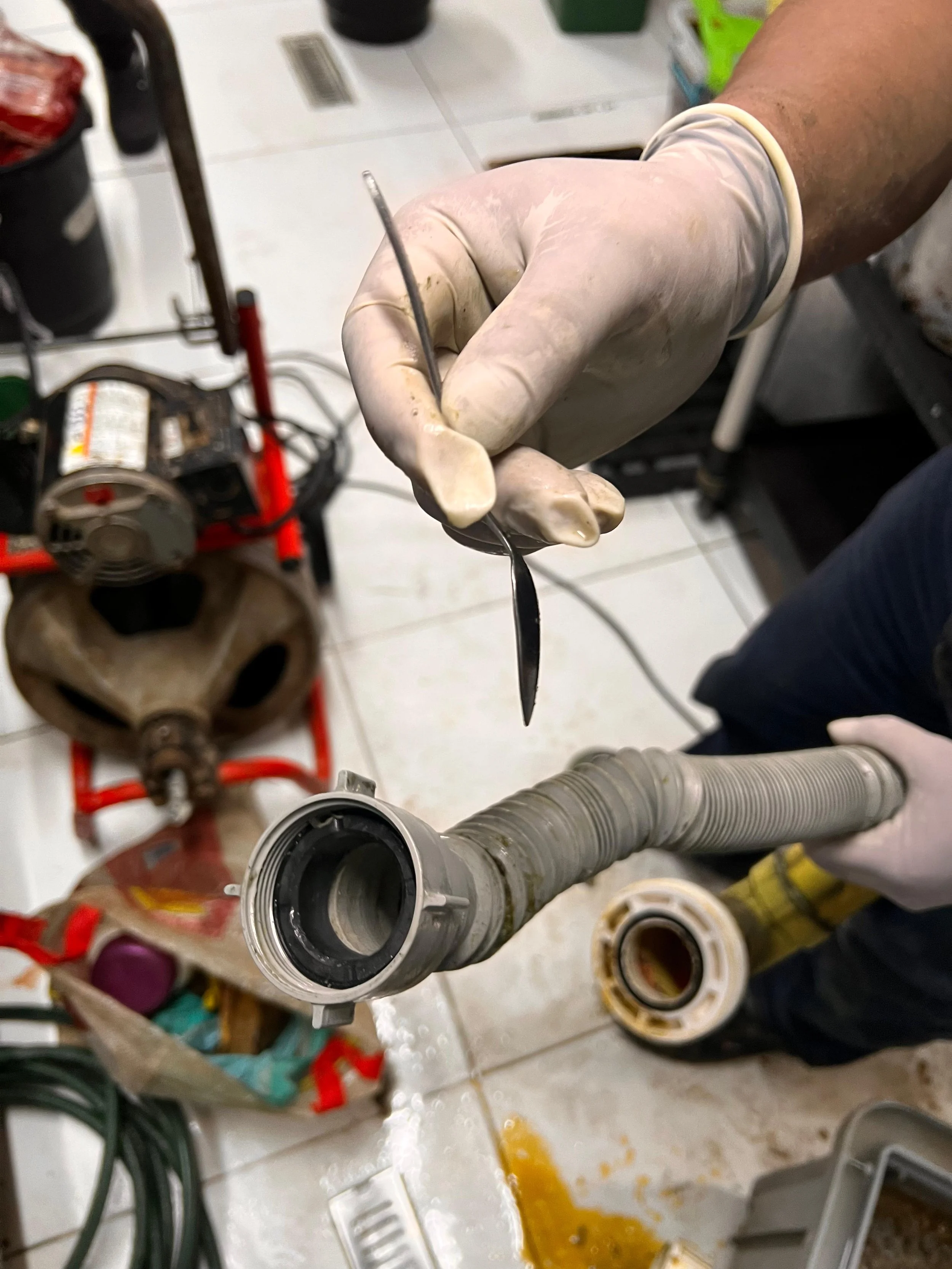 Mano con guantes sosteniendo una pieza de plomería y otra elemento similar en un taller de reparación de cañerías.