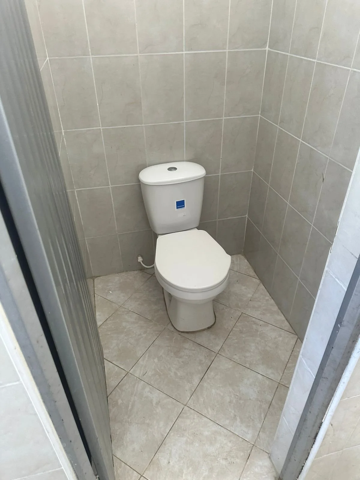 Inodoro blanco en un baño con paredes y suelo de azulejos beige.